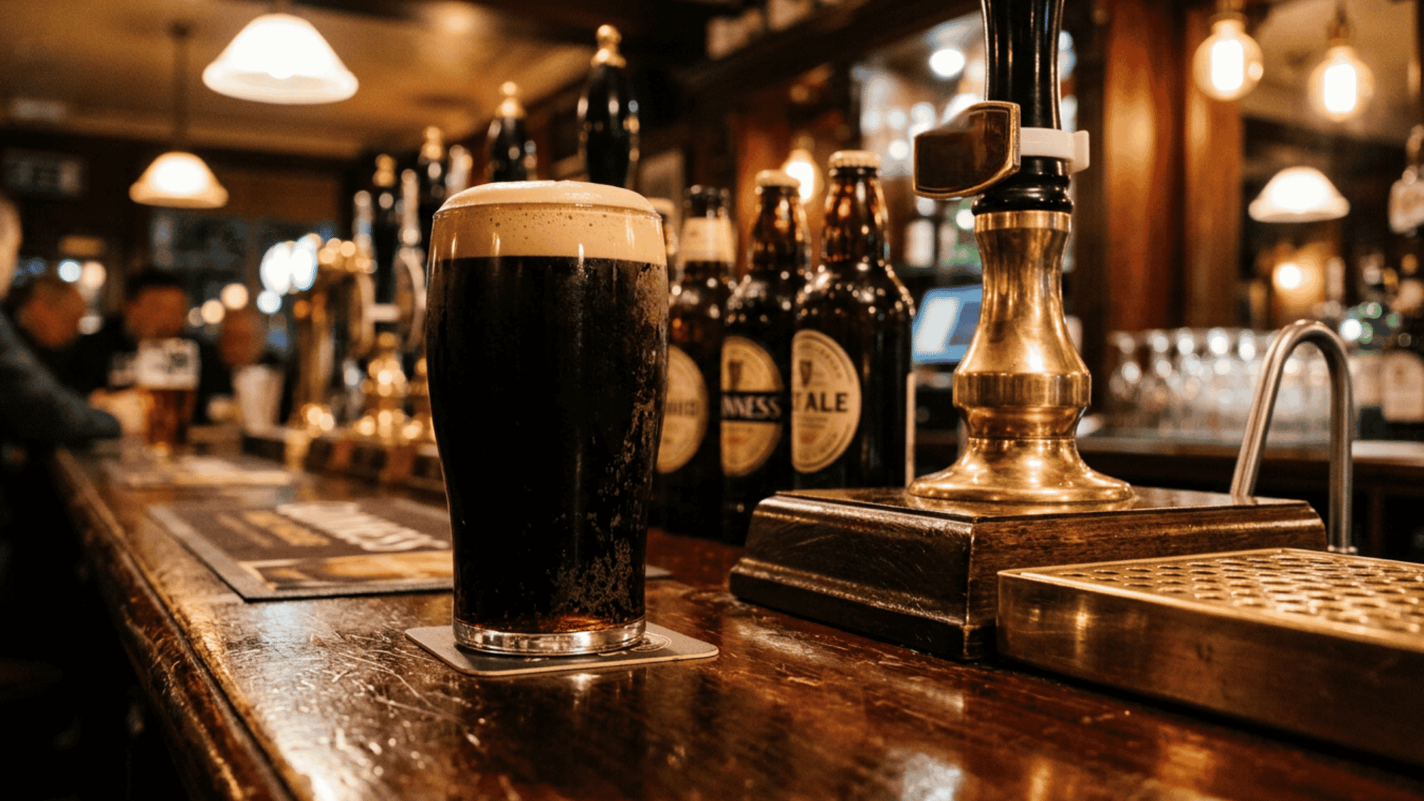 A freshly poured pint of traditional British cask ale in a nonic glass, showcasing a clear, bright amber color and a frothy head. The glass rests on a dark wood surface in a dimly lit, cozy pub setting.