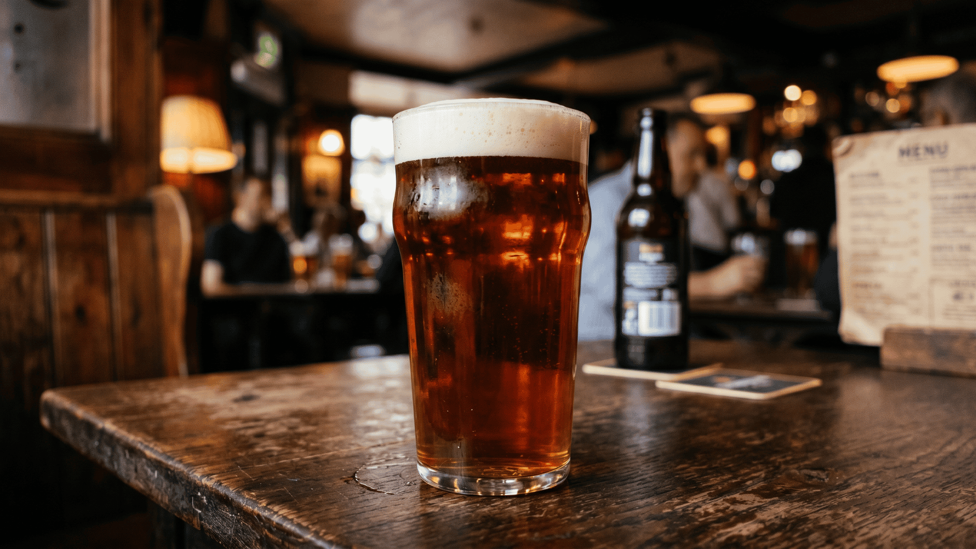 Close up of an imperial pint glass of dark beer in a traditional British pub bar.