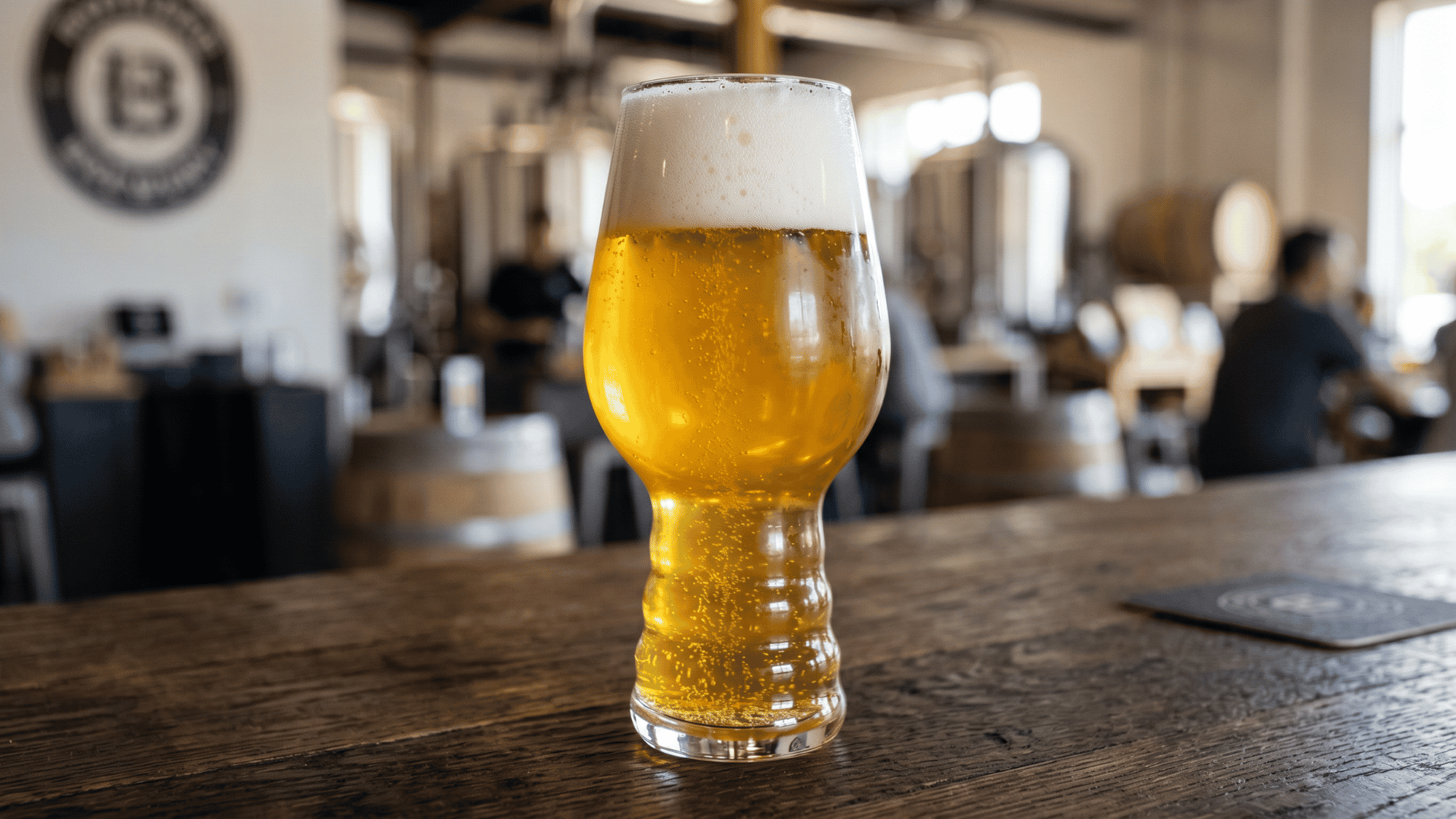 Close-up golden hazy beer in a stemmed glass on wooden table in craft brewery.