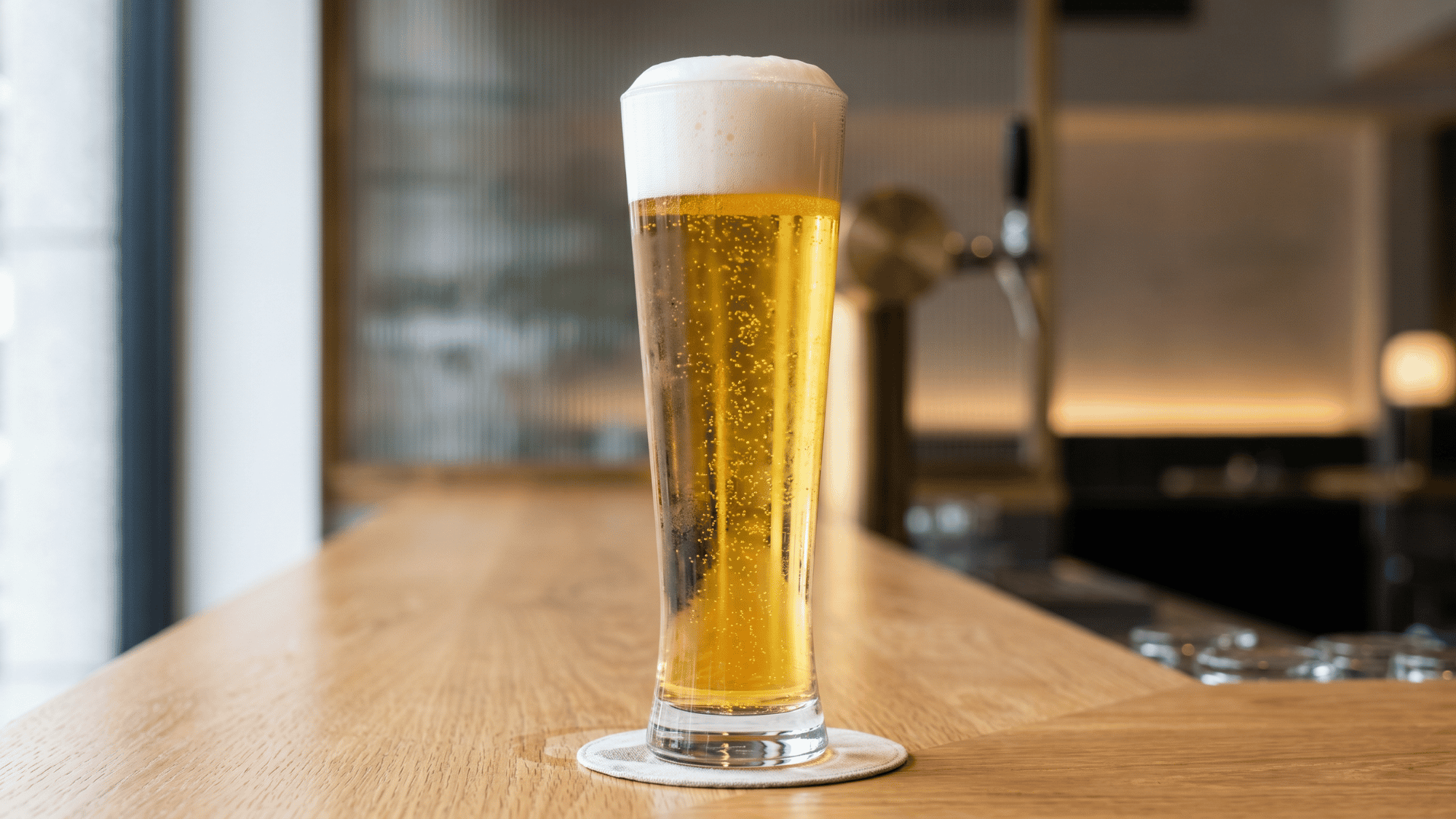 Pilsner beer glass with golden lager and foam head on a wooden bar counter table