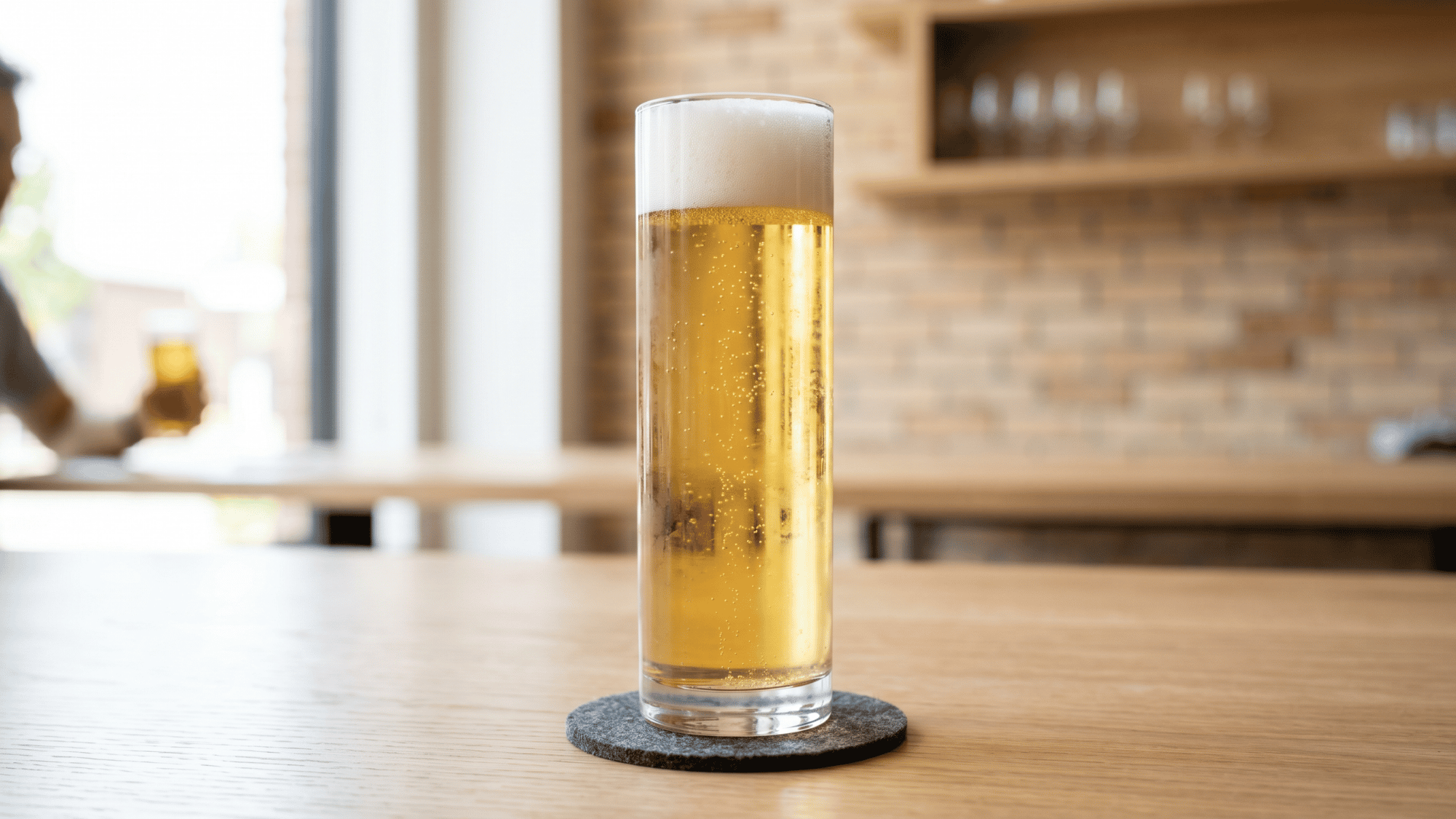 Golden pilsner in tall stange glass on coaster inside modern brewery bar