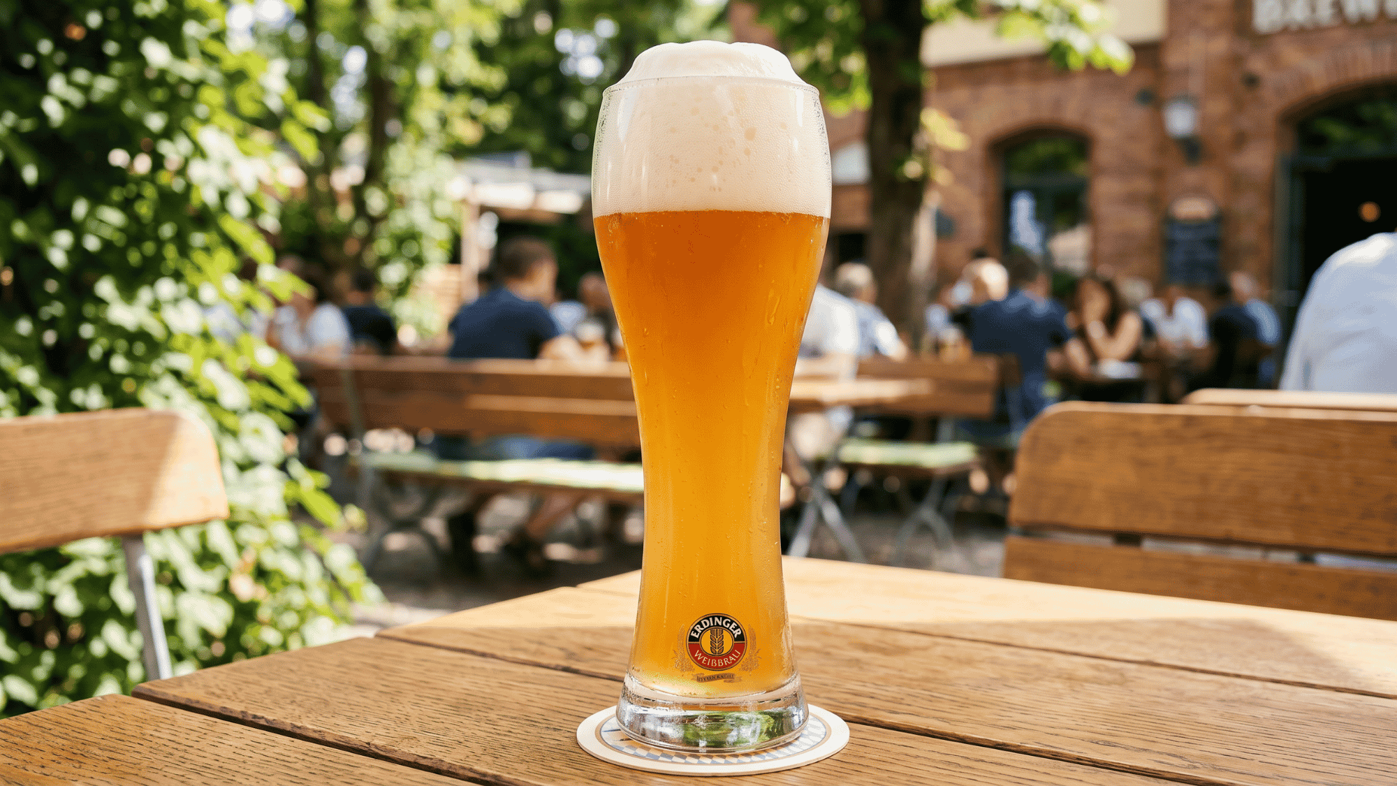Weizen wheat beer glass tall and cloudy with foam served in a German beer hall .
