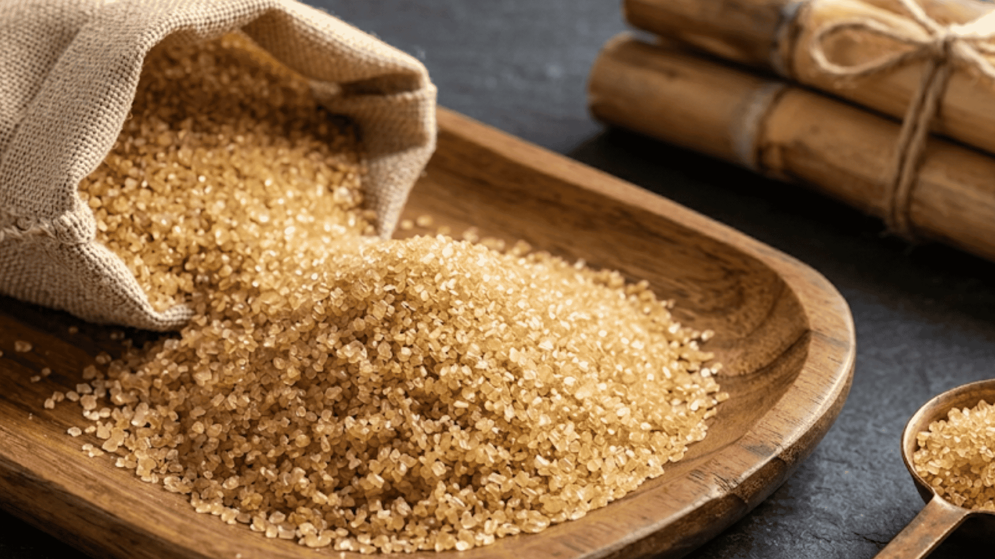 Fine evaporated cane sugar crystals in a white bowl placed next to raw sugarcane stalks