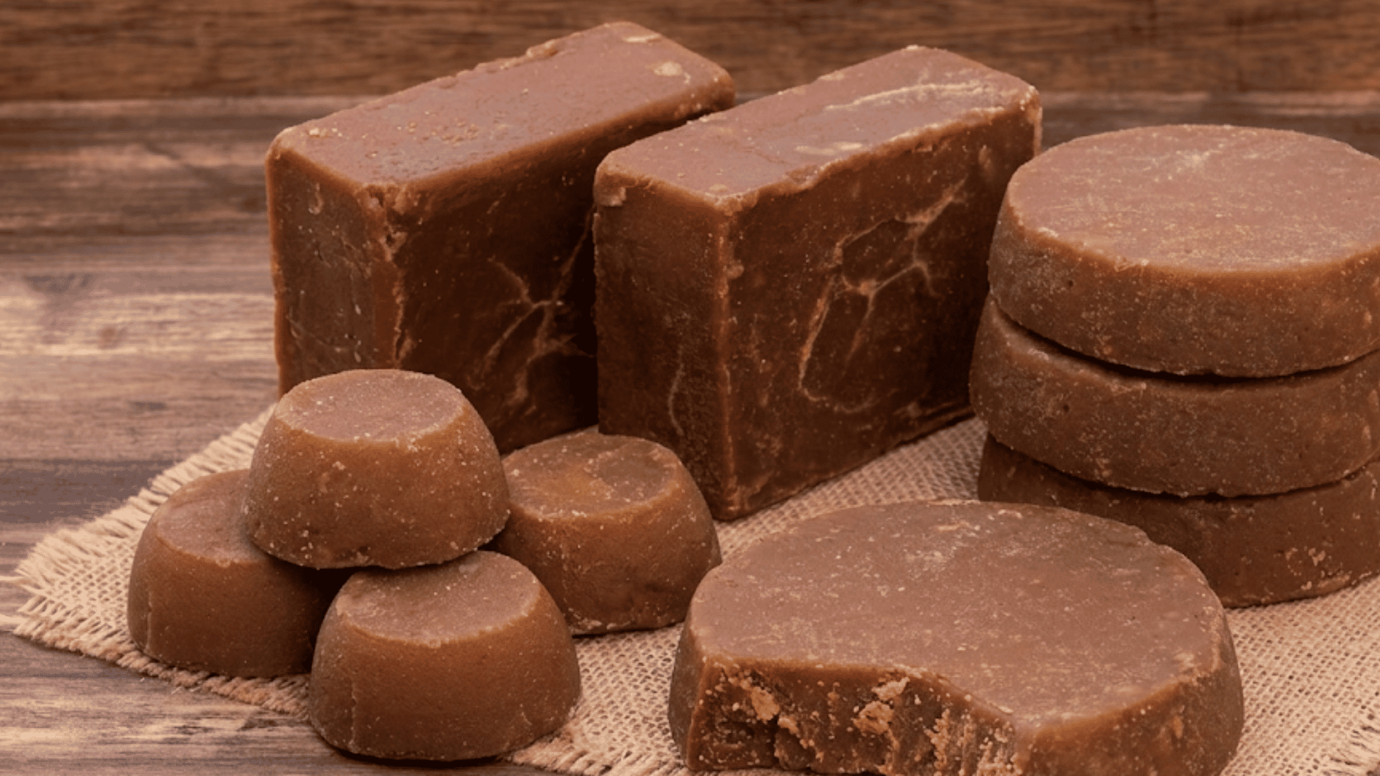 Solid dark brown panela blocks with raw sugarcane stalks on a rustic wooden surface in natural light