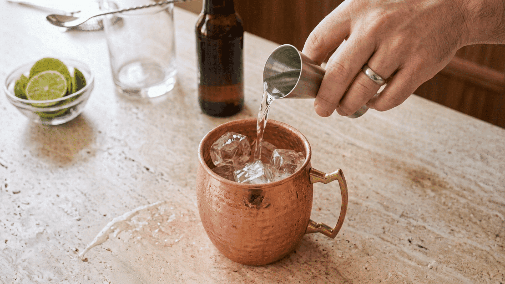 Hand pouring measured vodka over ice in a copper Moscow Mule mug.