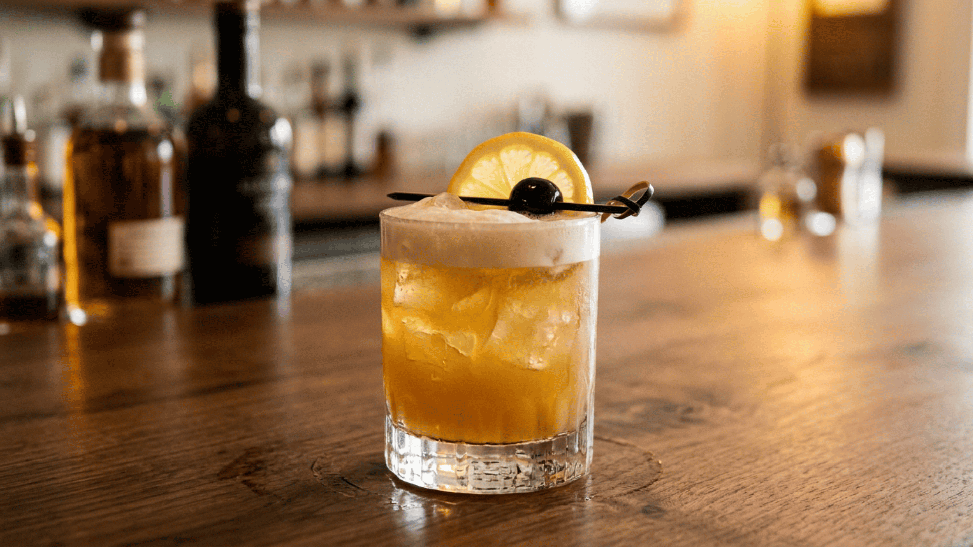 Amaretto Sour cocktail with foam, lemon slice, and cherry garnish.