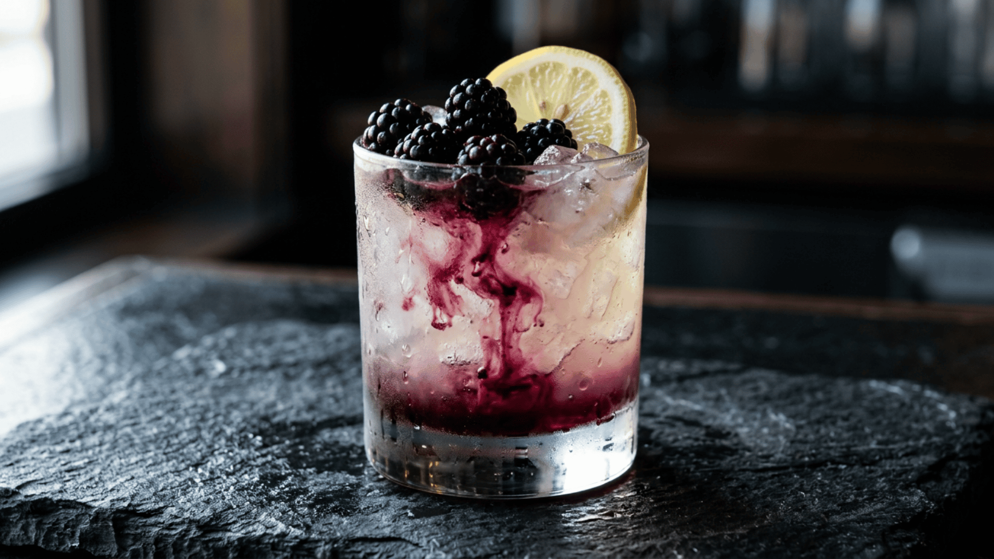 Bramble cocktail with blackberries, lemon, and crushed ice in a rocks glass