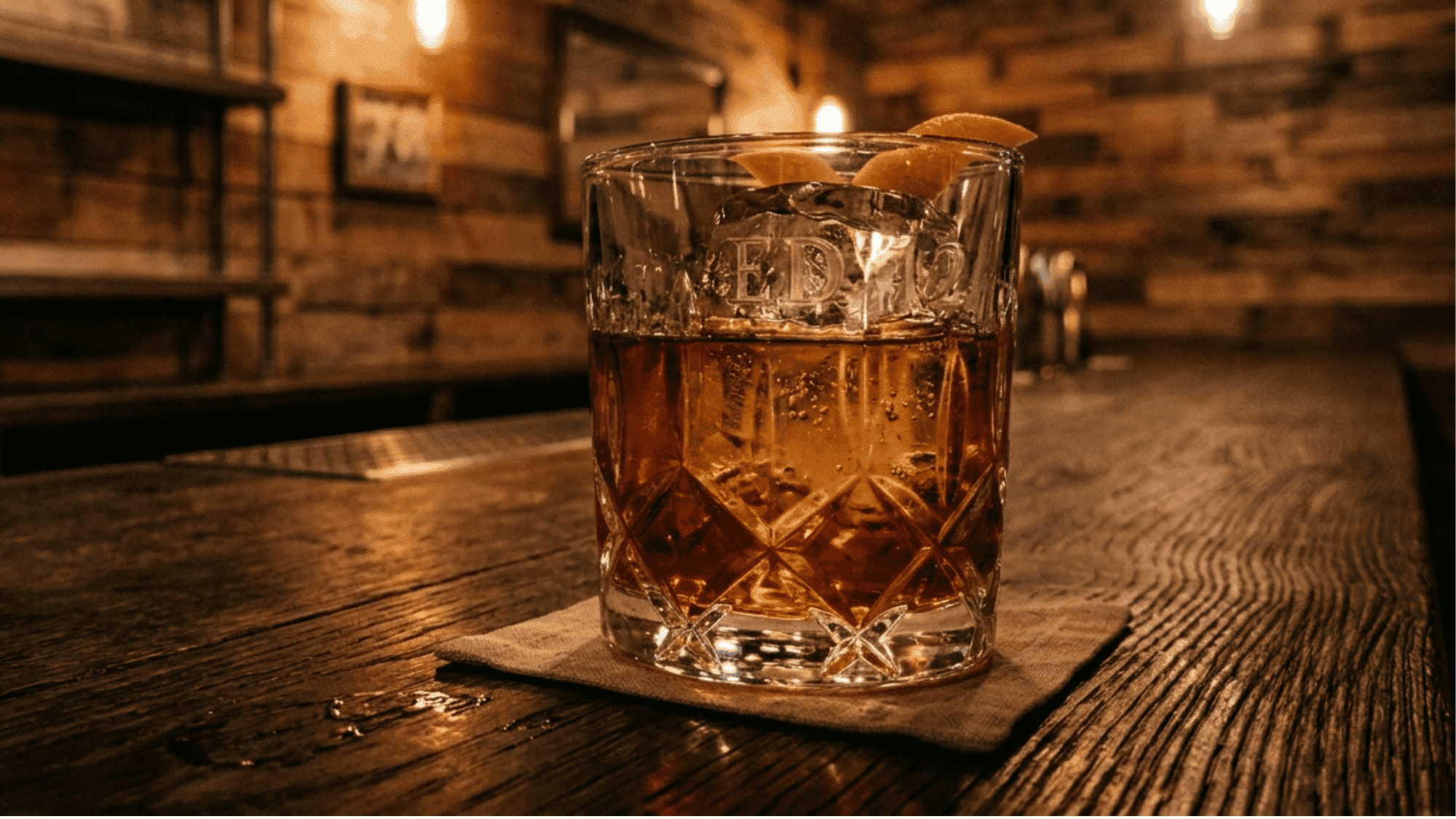 Glass of dark rum on a wooden bar with warm lighting and orange peel garnish