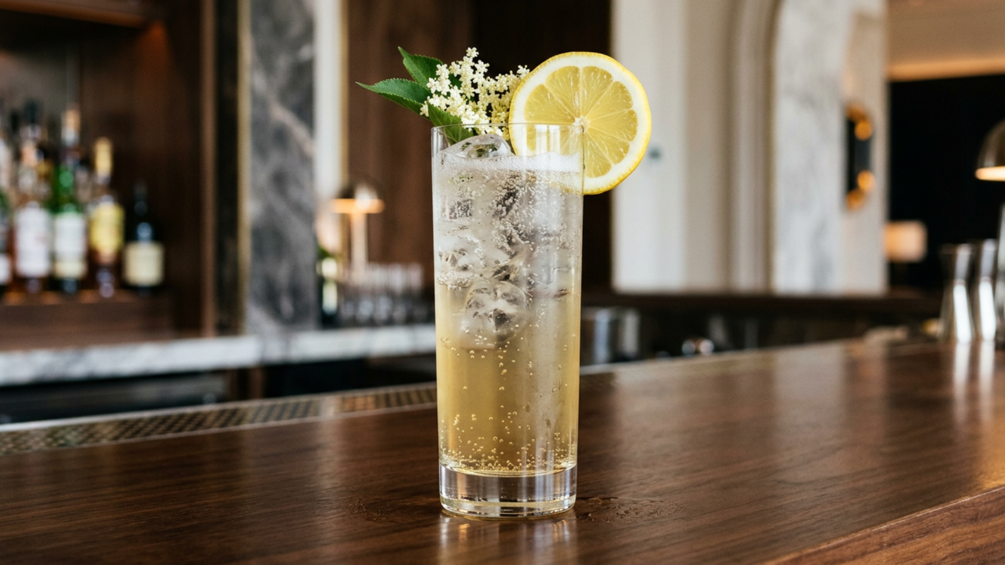 Elderflower Collins with lemon, blossoms, and ice in a tall glass at a bar