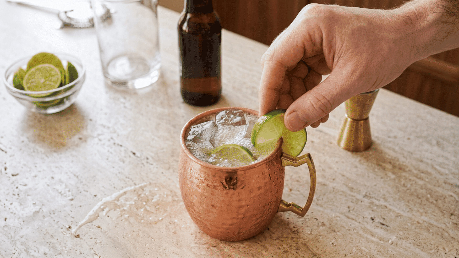 Hand garnishing a fizzy Moscow Mule in a copper mug with a fresh lime wheel.