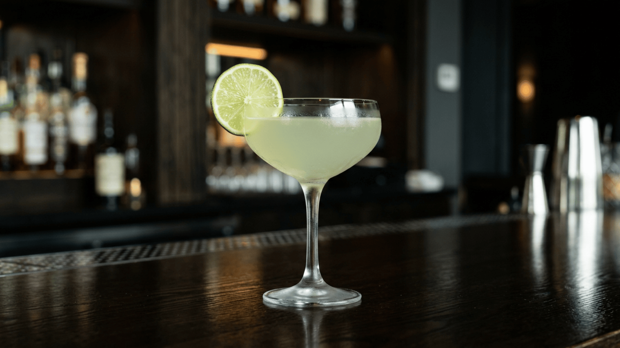 Gin gimlet in a coupe glass with a fresh lime wheel on a dark bar counter