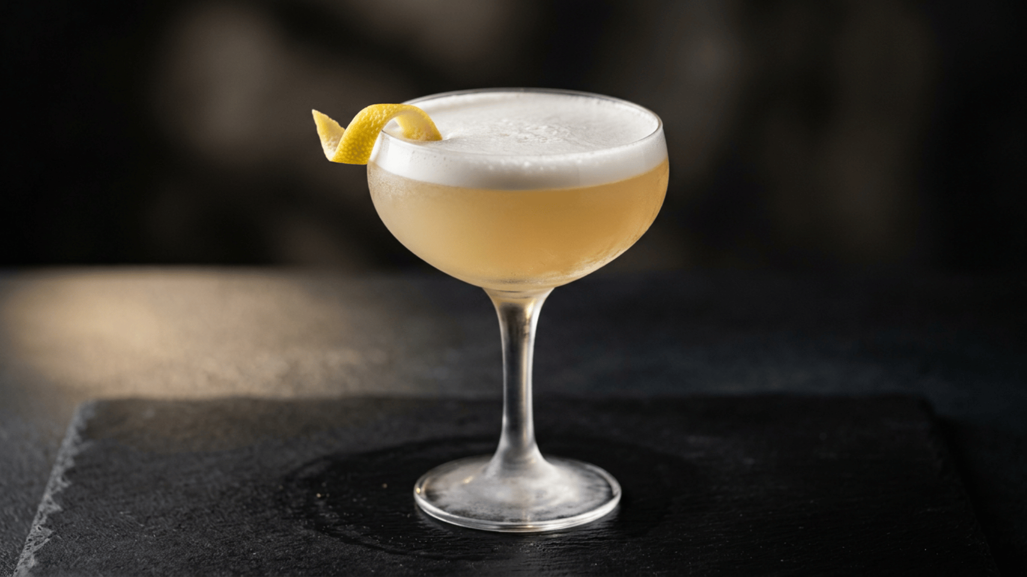 Gin sour with a foamy top and lemon twist in a chilled coupe glass