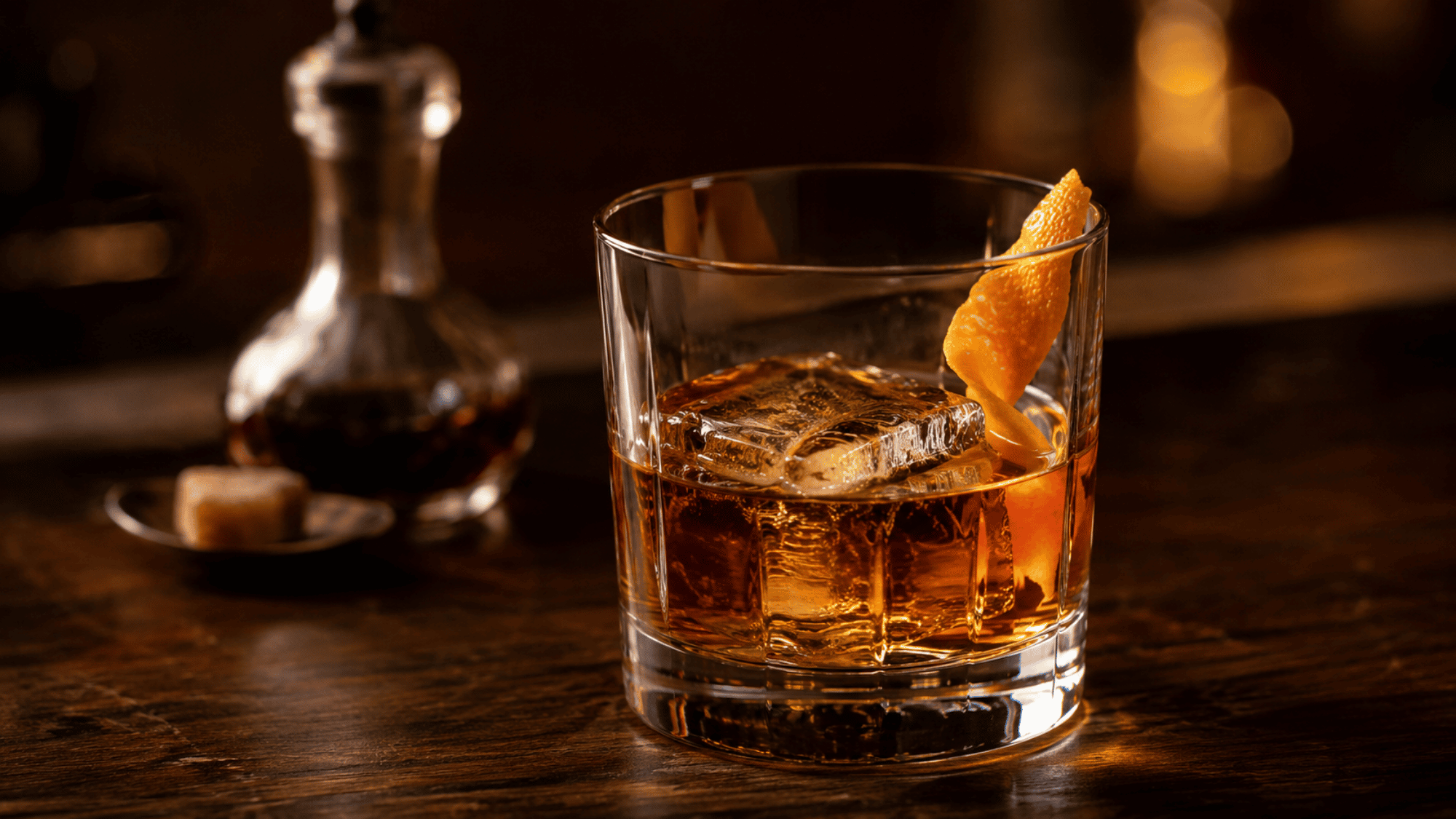 Gold Rush cocktail with ice and orange peel on a warm wooden bar