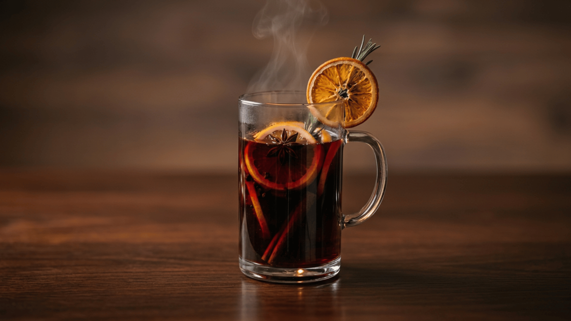Steaming mulled wine in a glass mug with citrus and spices on a rustic wooden table.