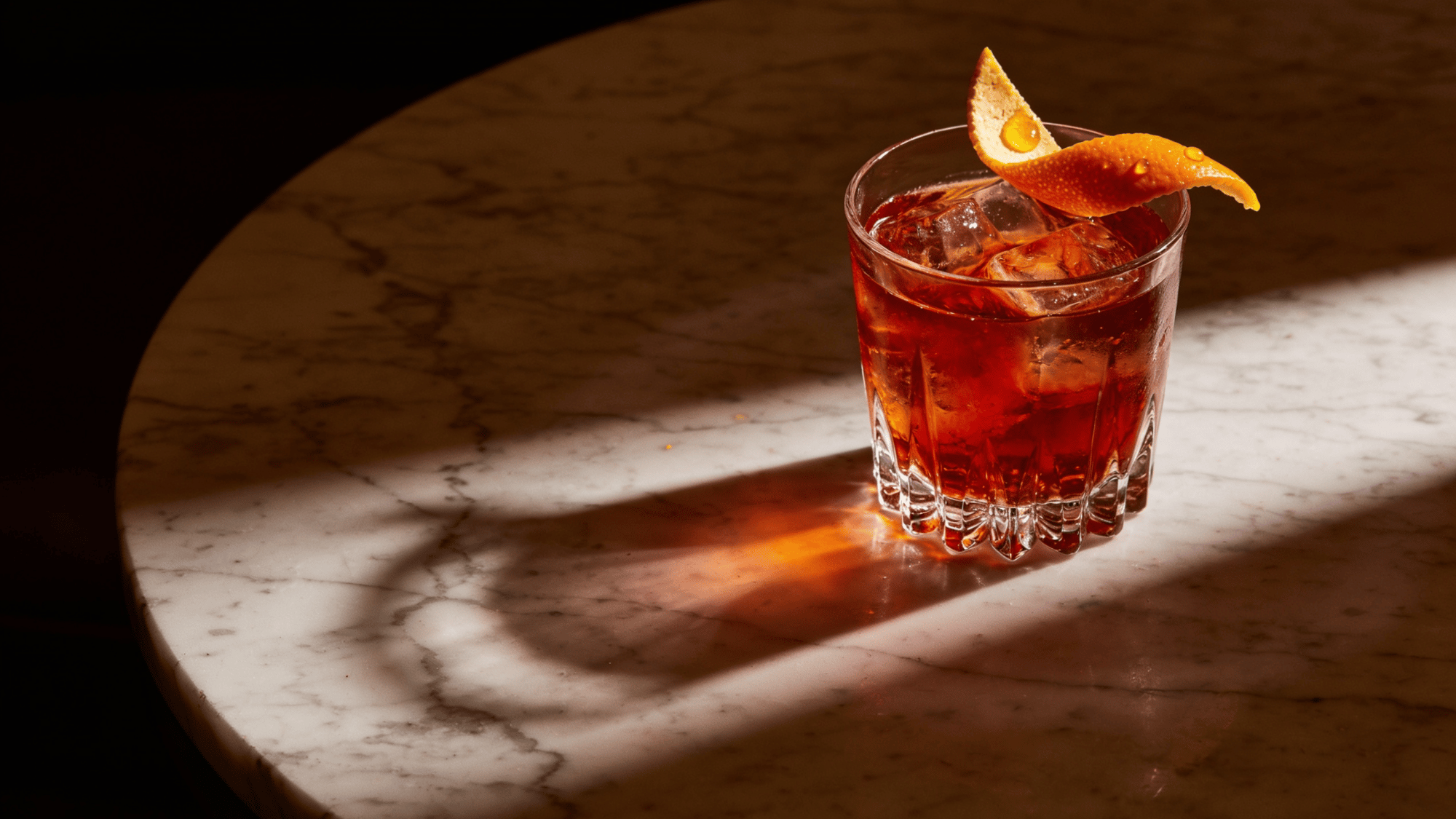 negroni cocktail with orange peel over ice on a sunlit marble table