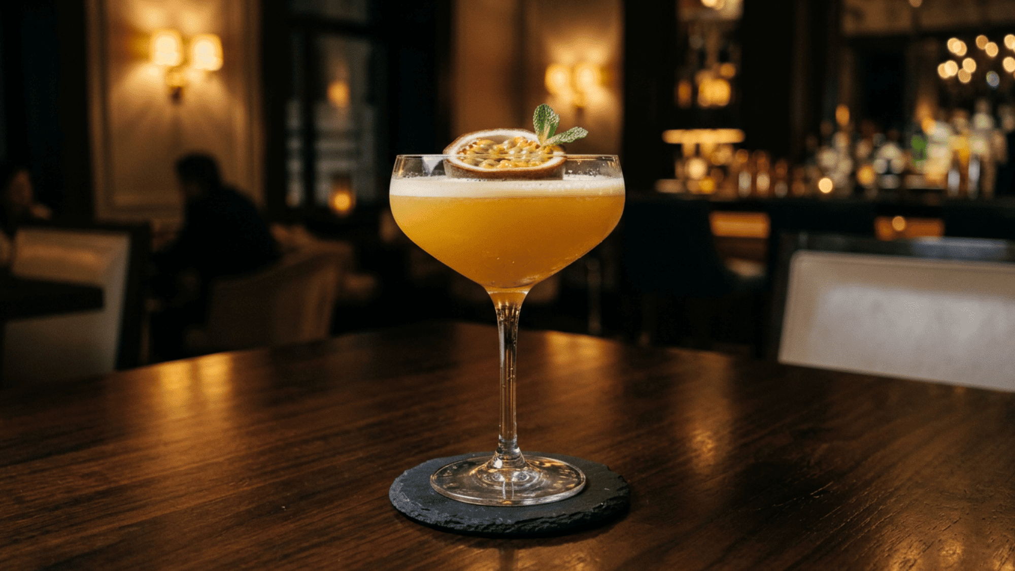Passion fruit martini in a coupe glass with a passion fruit garnish on a dark bar
