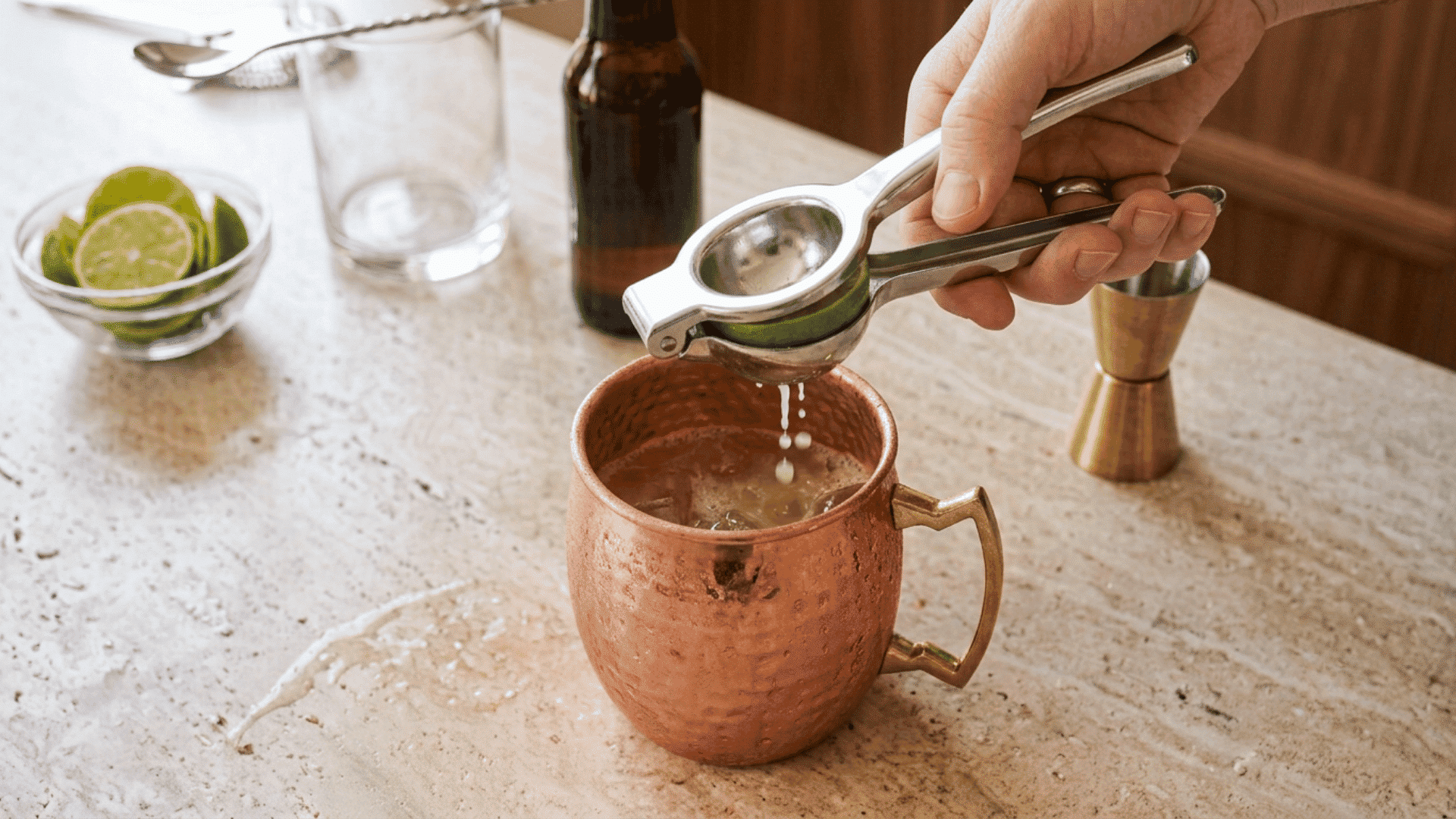 Hand squeezing fresh lime juice into a copper mug with a citrus press.