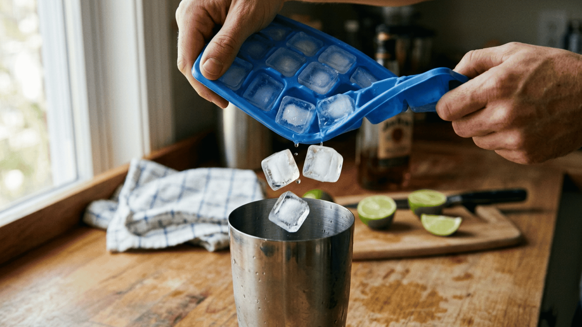 Adding large ice cubes into a cocktail shaker to chill a drink.
