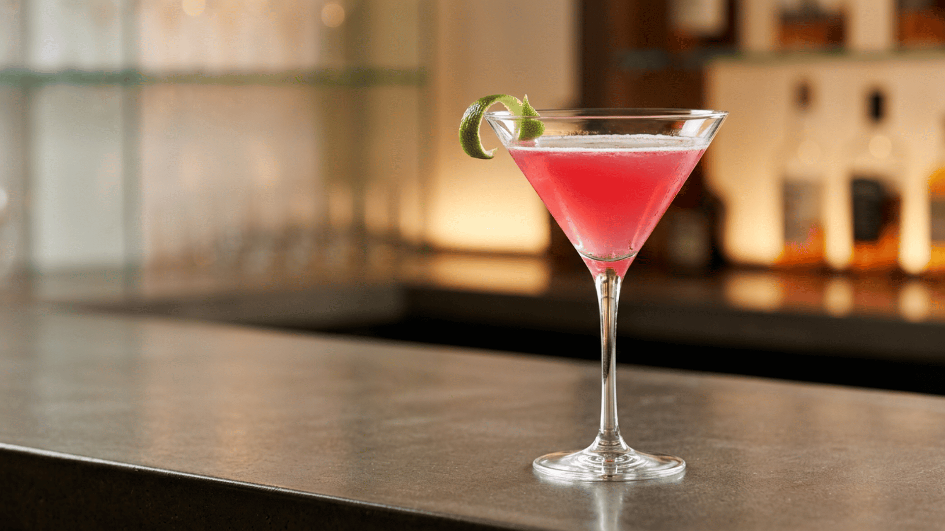 Pink Cosmopolitan cocktail in a martini glass with lime twist garnish.