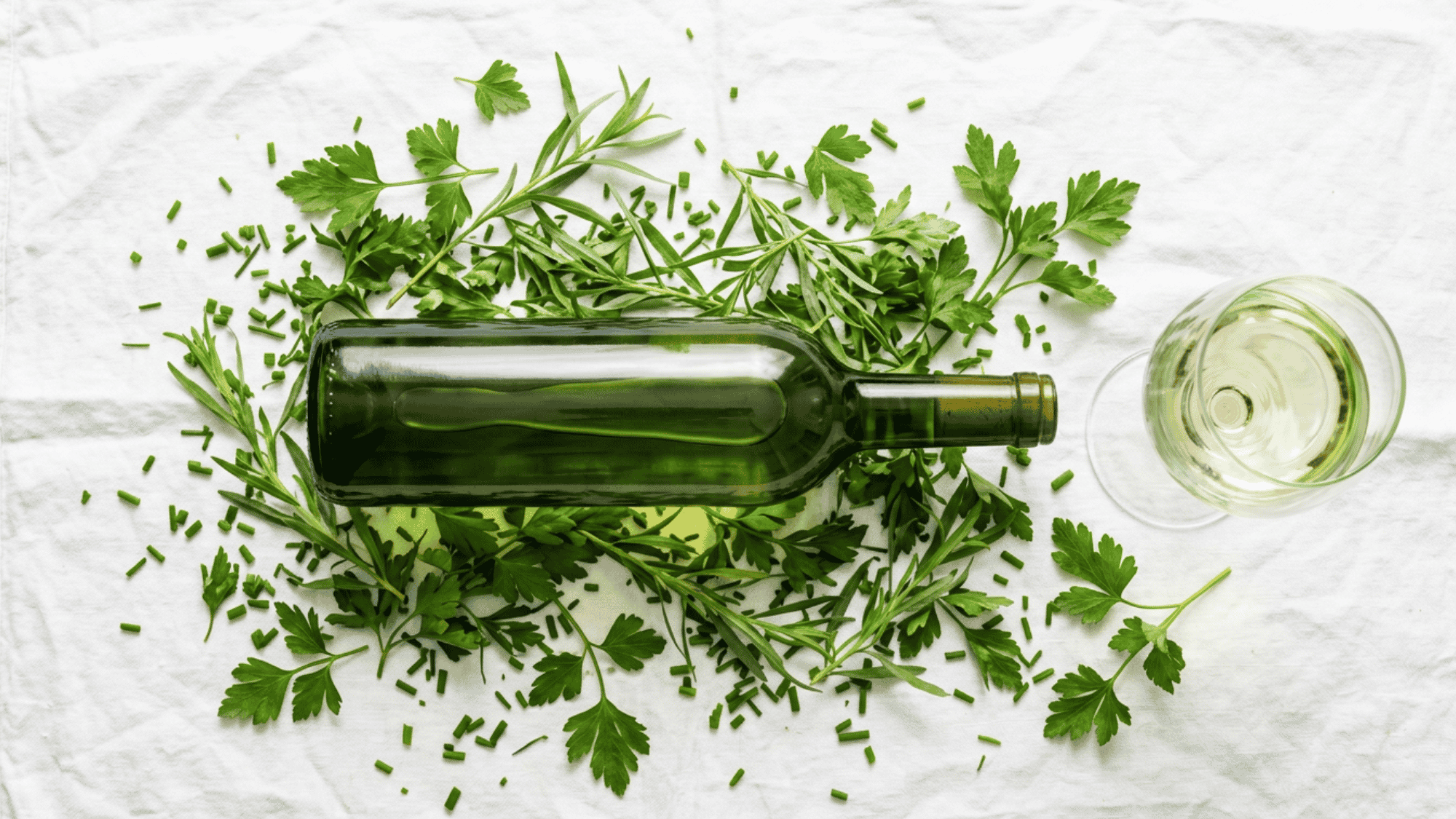 Top view of Sauvignon Blanc bottle and glass surrounded by fresh green herbs.