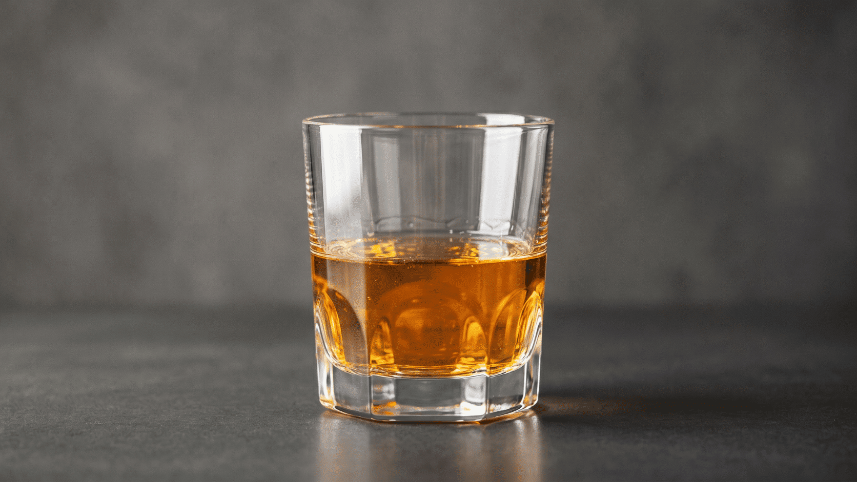 Close-up of a glass of Scotch whisky with amber liquid on a dark background, soft studio lighting.