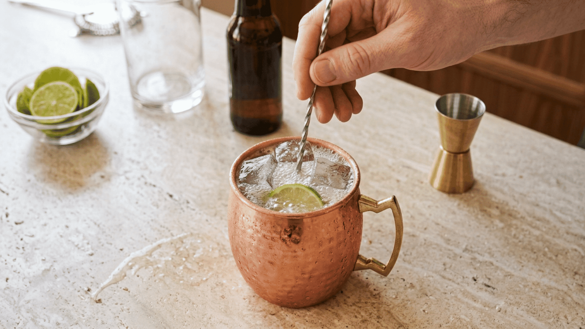 Hand gently stirring a chilled Moscow Mule with ice in a copper mug.