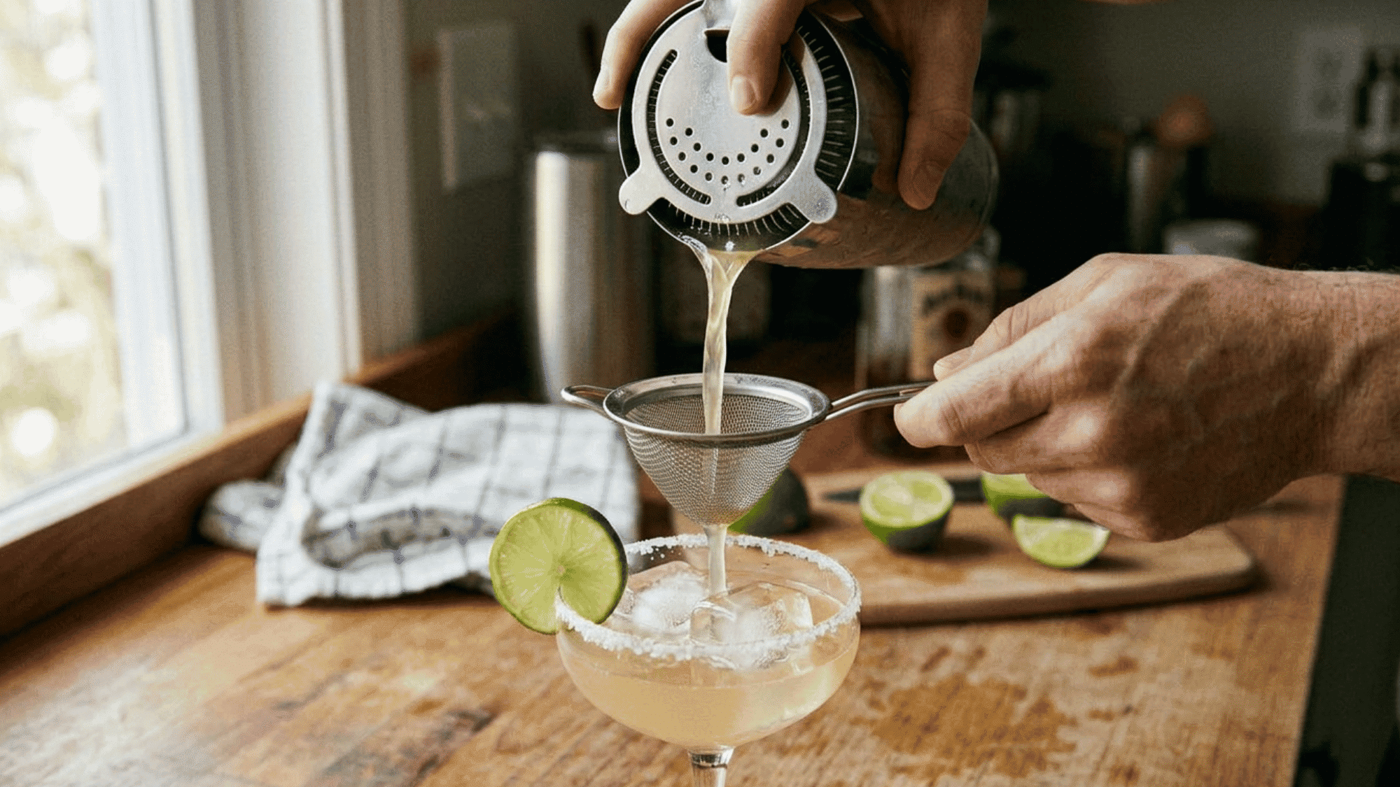 Pouring a cocktail through a fine mesh strainer into a chilled coupe glass.