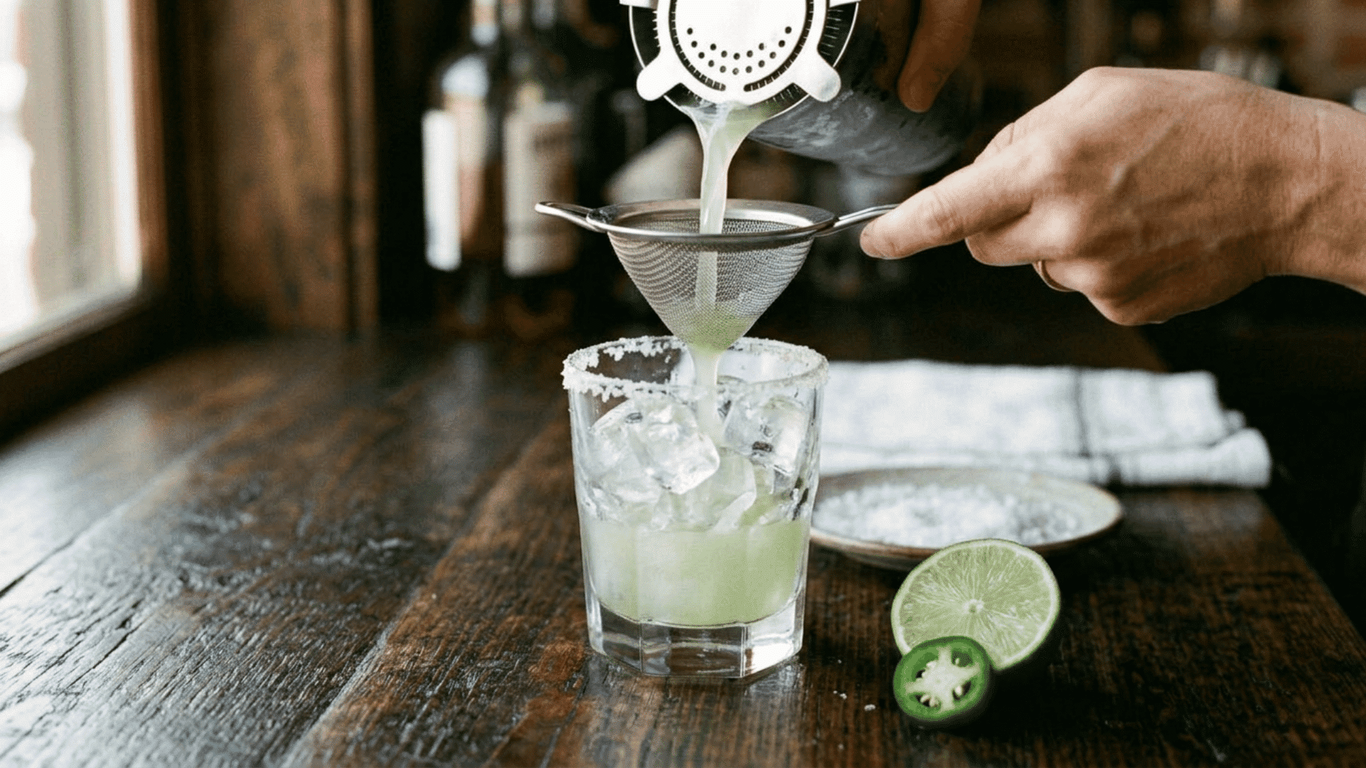 Margarita being strained into a glass with fresh ice and garnish