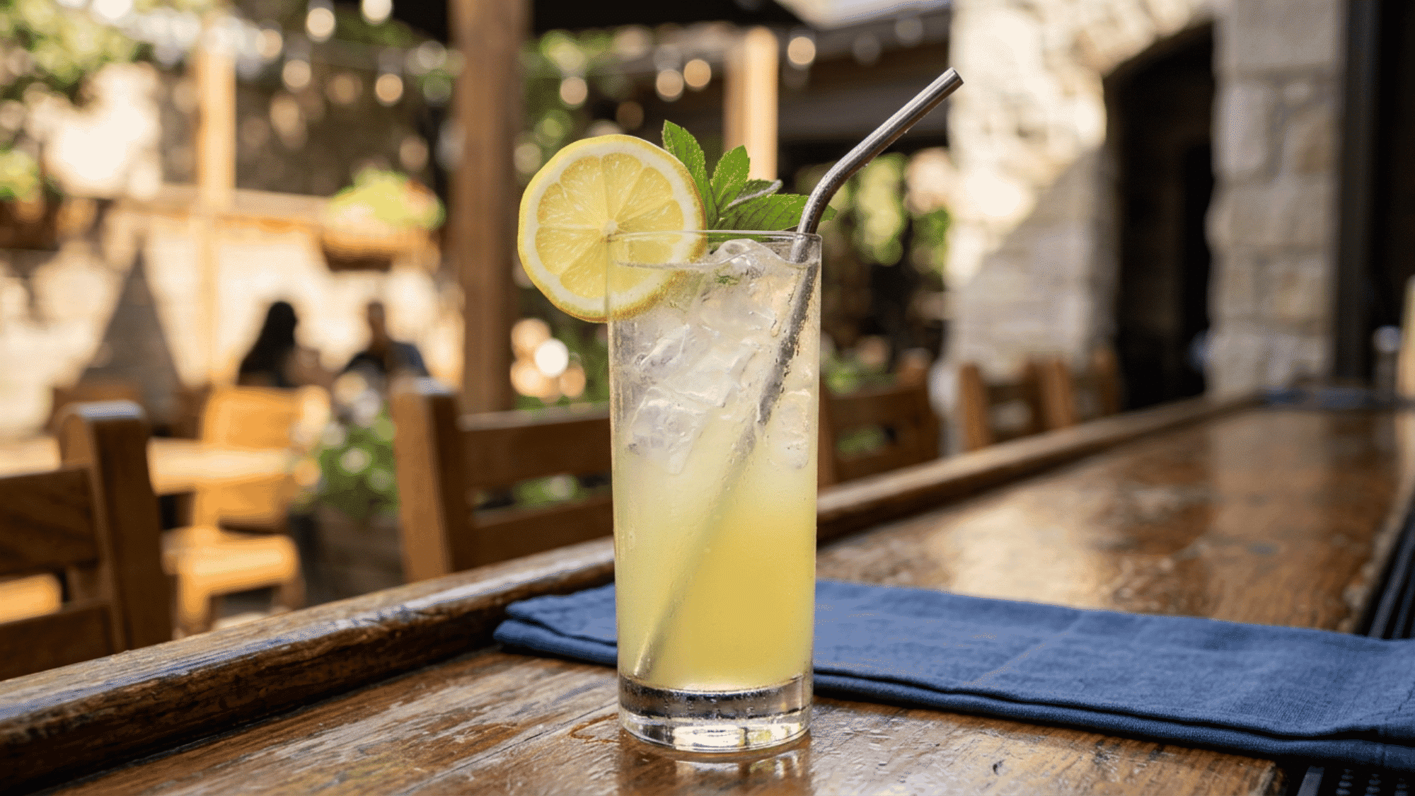 Tequila lemonade with lemon, mint, and ice on a sunny patio bar