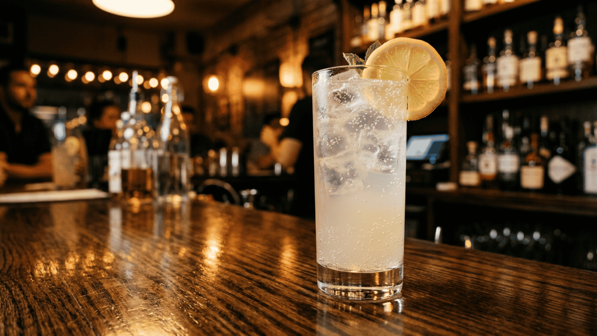 Tom Collins cocktail with lemon garnish on a warm bar counter