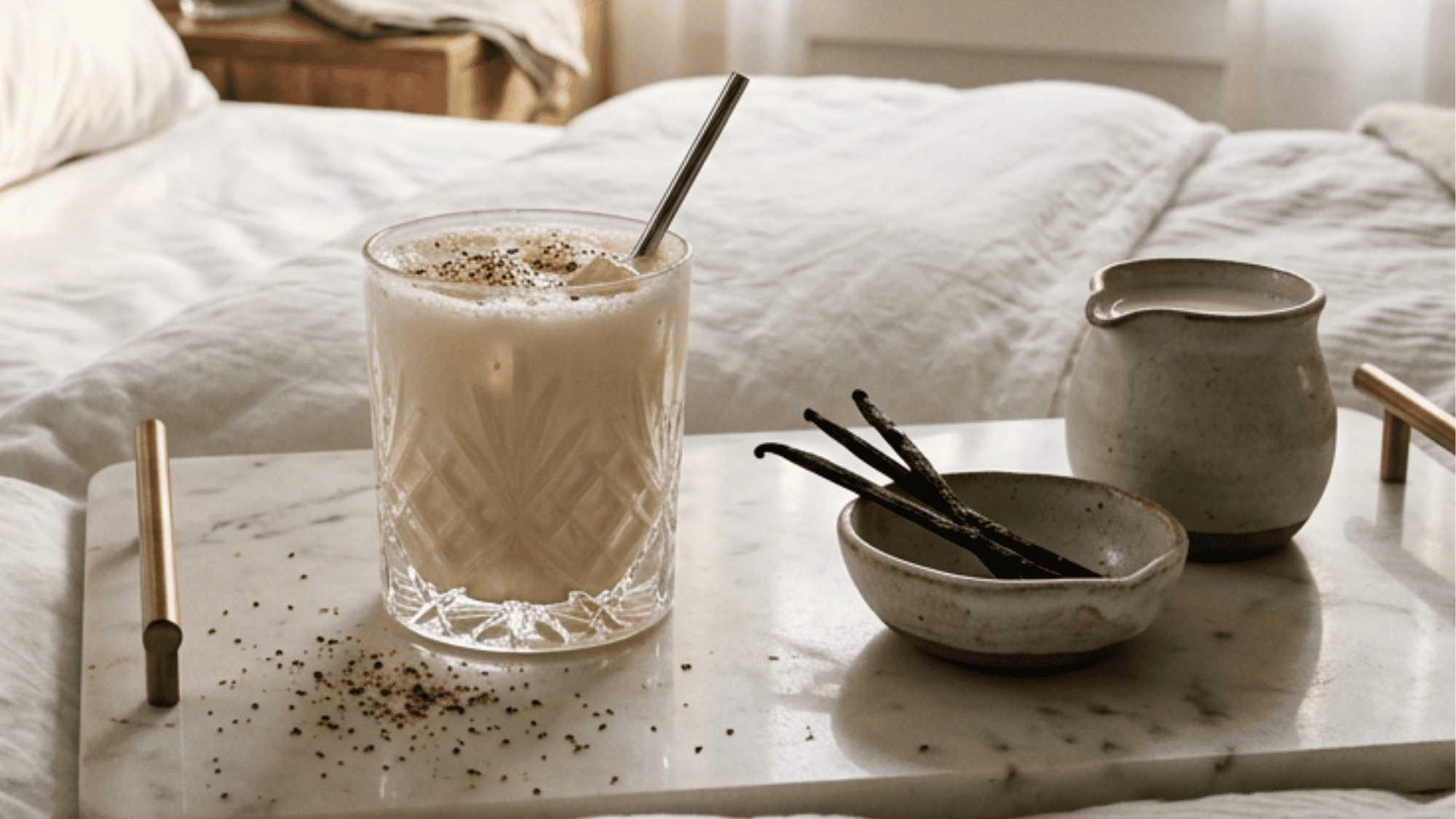 Vanilla bourbon milk punch on a breakfast tray beside vanilla beans in a cozy bedroom.