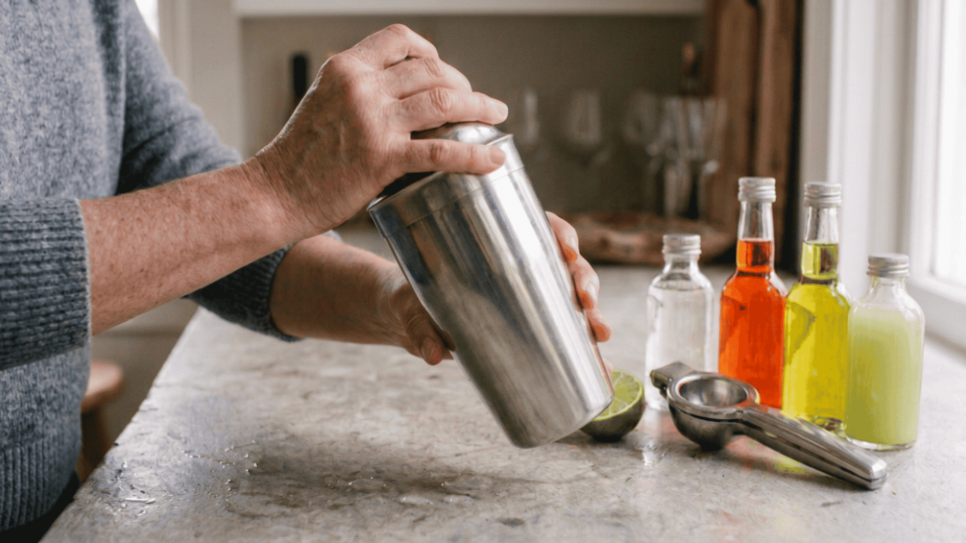 hands shaking a chilled metal cocktail shaker filled with ice on a home bar counter