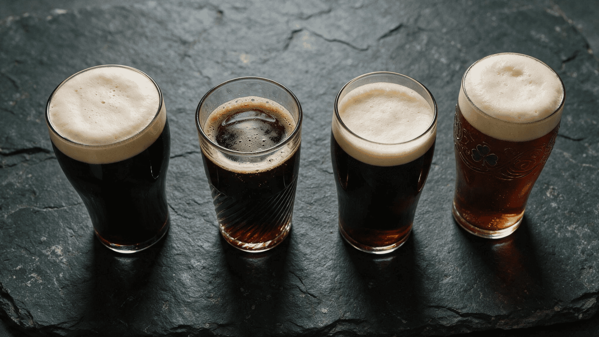 Three different sized glasses of dark stout beer arranged side by side on a white marble surface