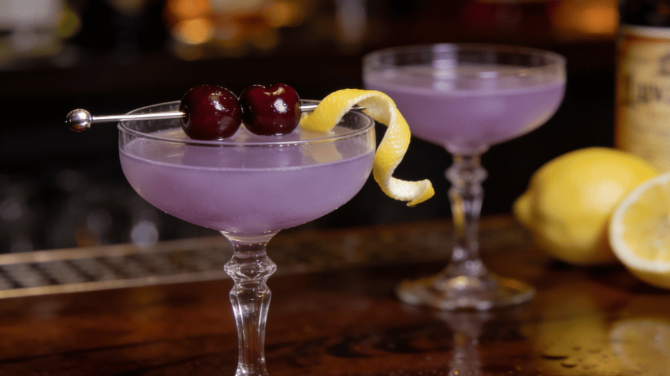 aviation cocktail with cherries and lemon twist in coupe glass on a polished wooden bar