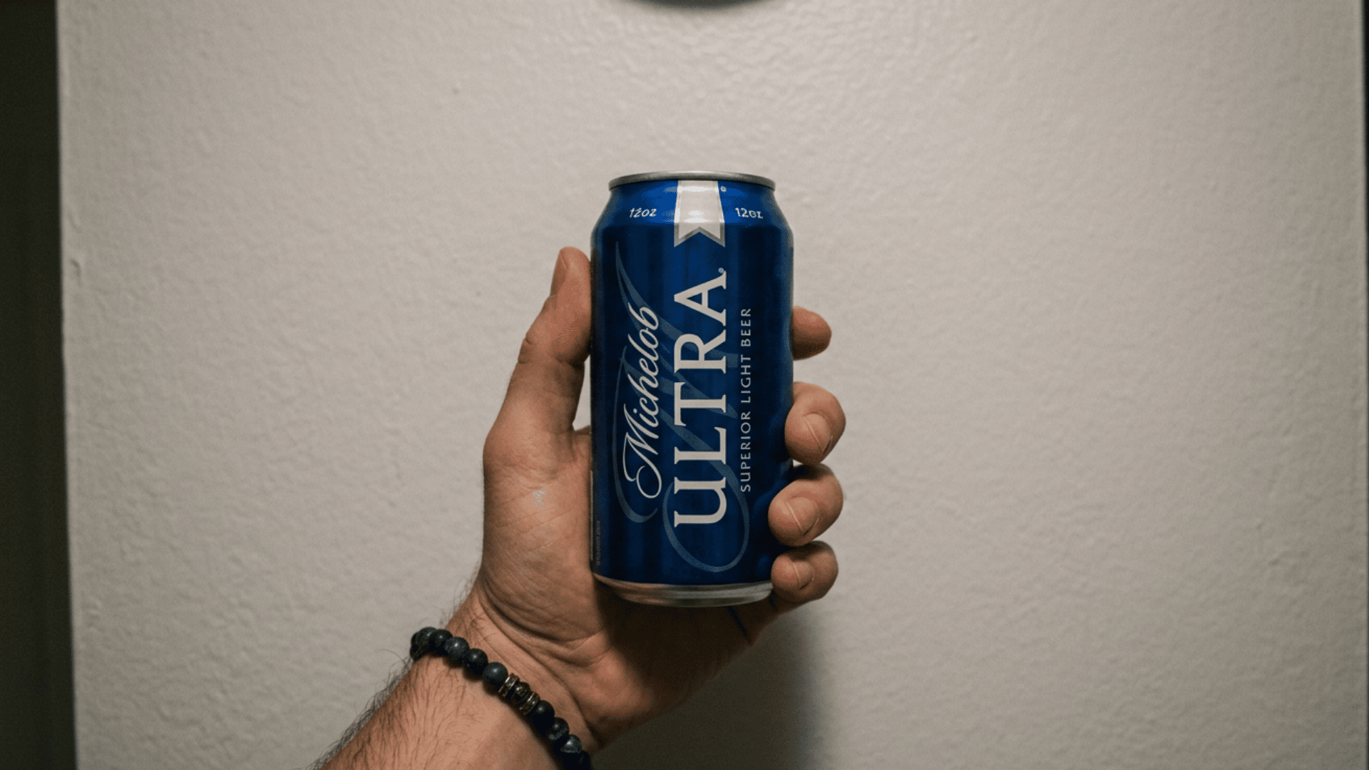Hand holding a Michelob ULTRA beer can against a plain background indoors on a neutral wall viewshot