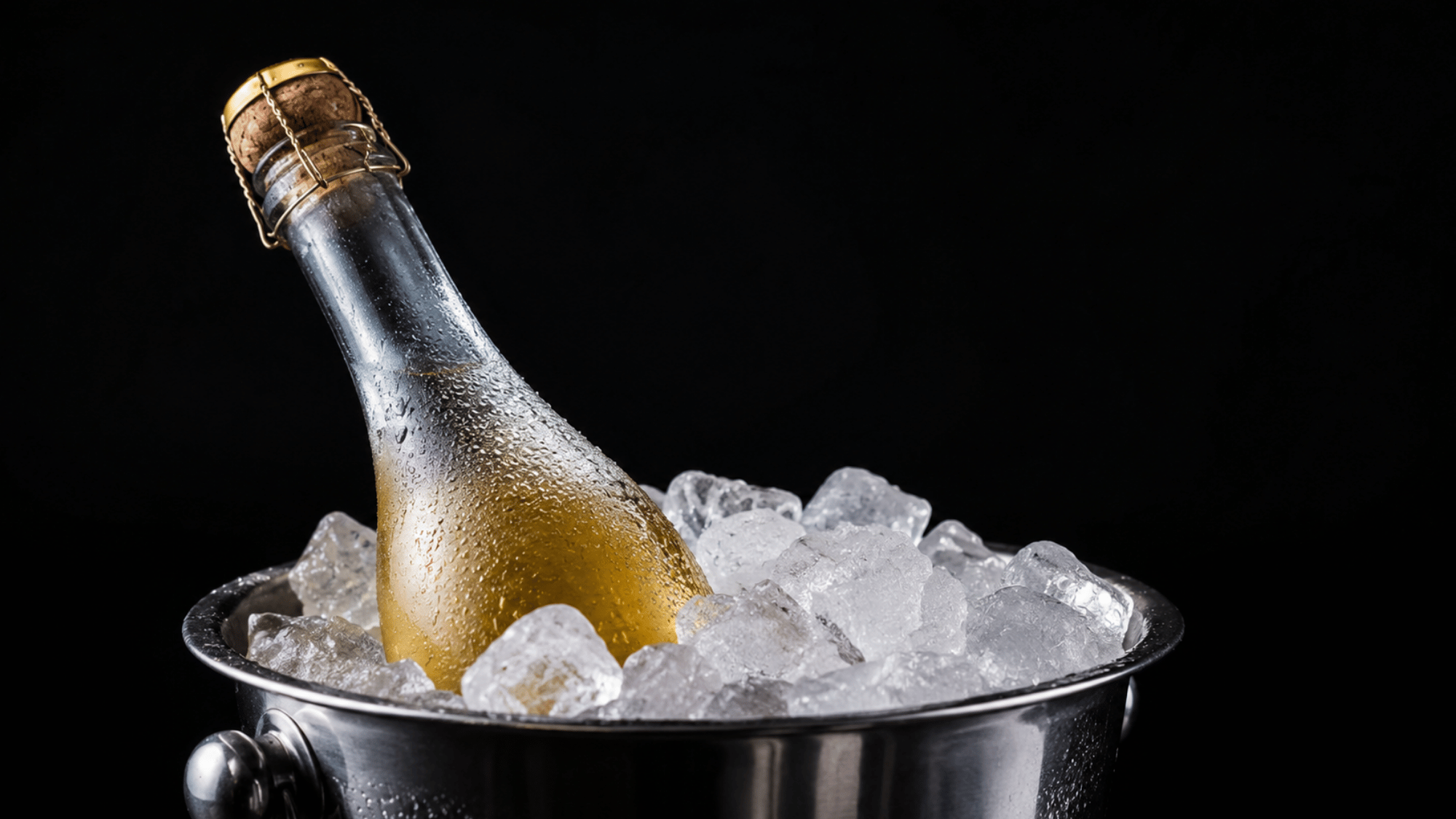 Chilled sparkling wine bottle resting in a metal ice bucket filled with ice against a black background.