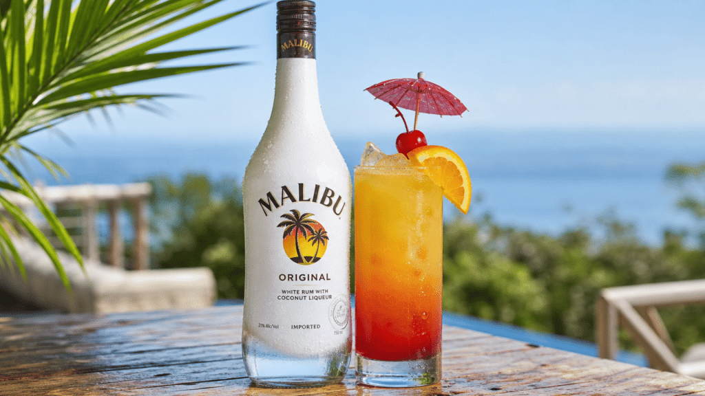 malibu original bottle beside a tropical orange cocktail on a bright, sunny seaside patio.