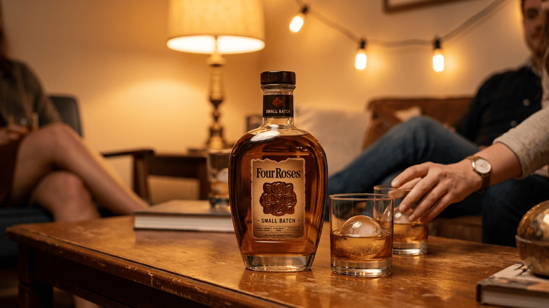 four roses small batch bourbon bottle on a coffee table with two poured glasses and warm lights