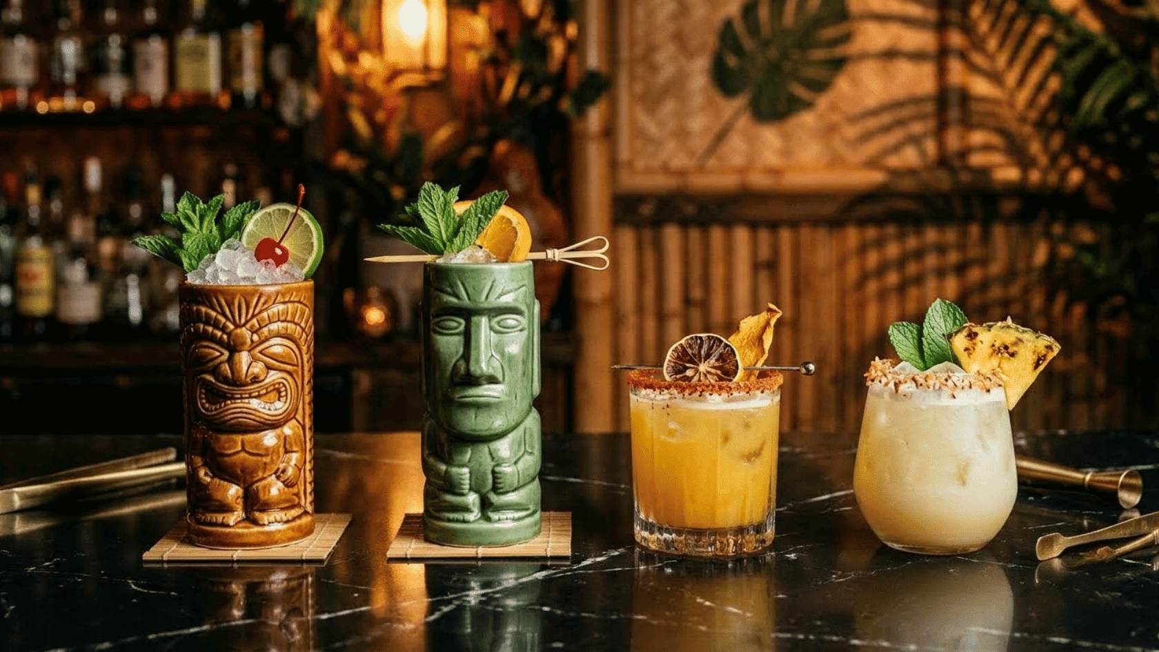 four tropical cocktails with fruit and mint garnishes displayed on a bar counter