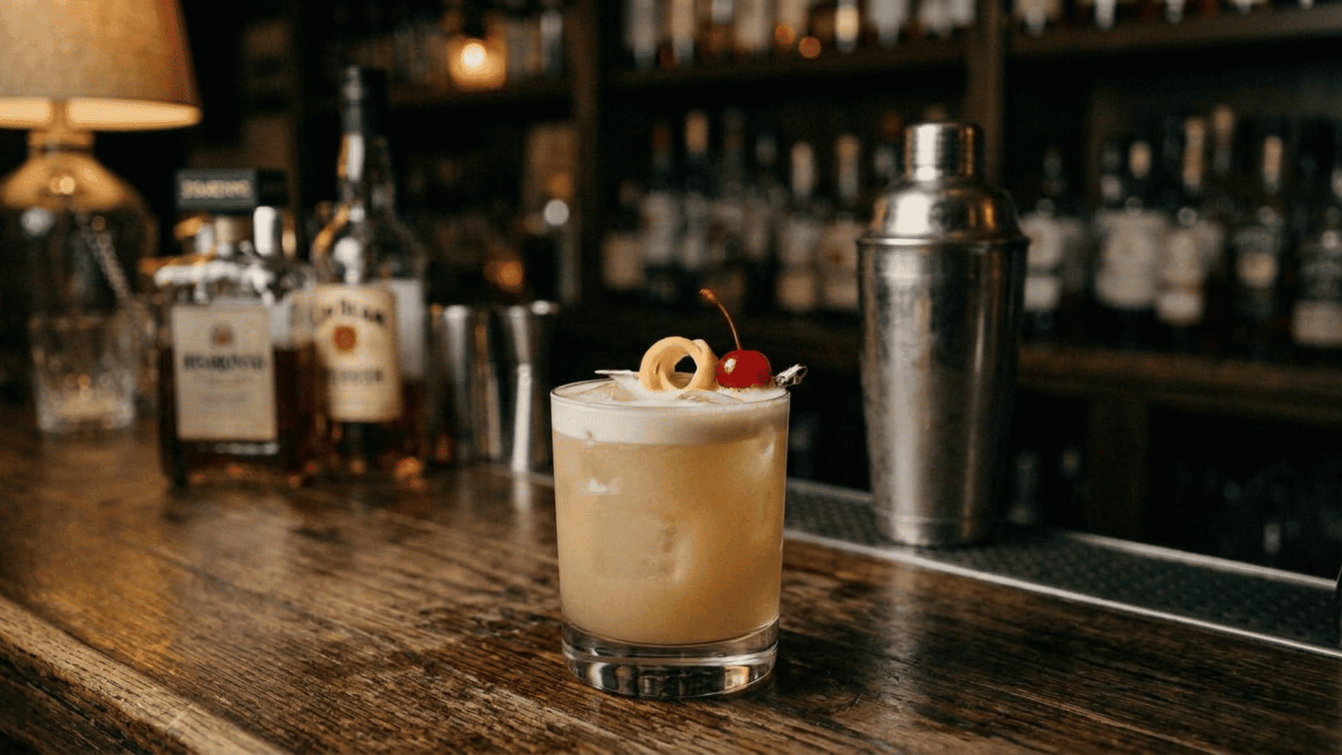 chilled amaretto sour with creamy foam, lemon curl, cherry, and shaker behind