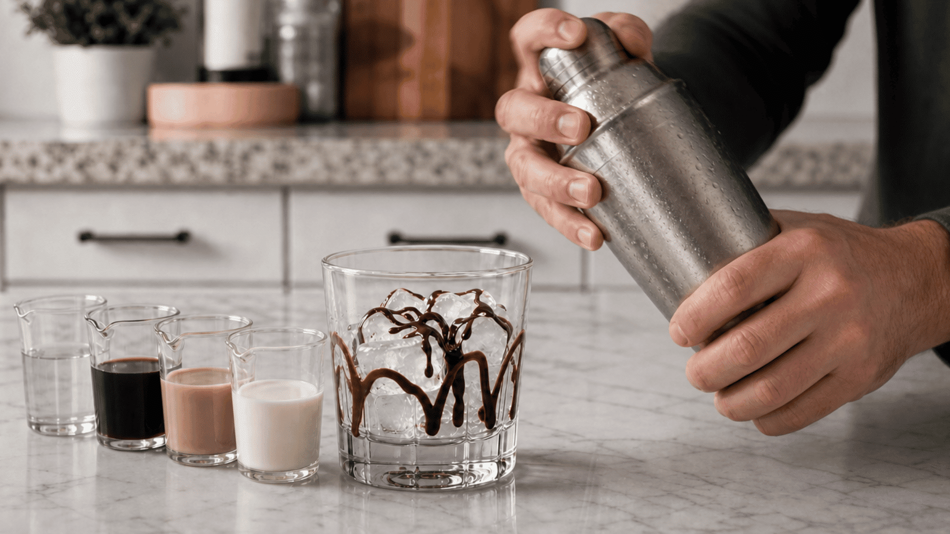 hands shaking a chilled cocktail shaker beside an ice-filled glass for a mudslide recipe