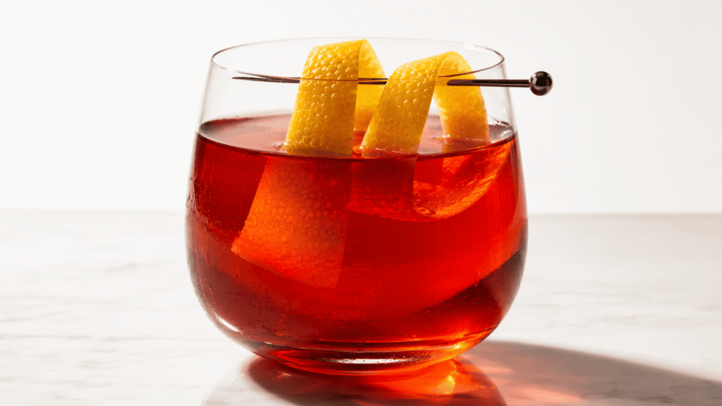 Sazerac cocktail garnished with a lemon peel in a rounded glass