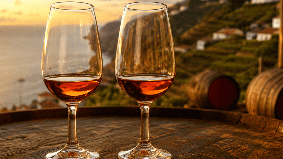 Two glasses of Madeira wine overlooking terraced vineyards and the coastline at sunset