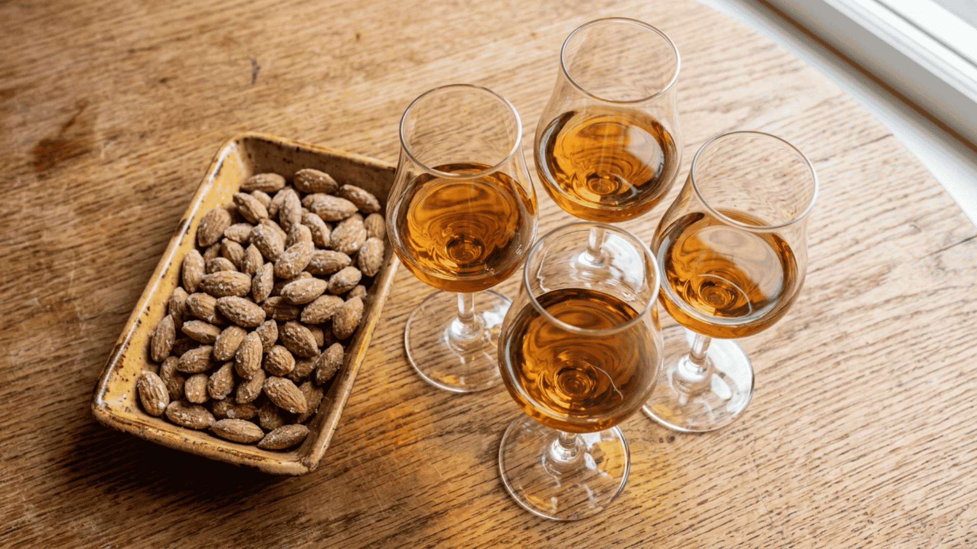 four glasses of amber sherry beside roasted almonds on a rustic wooden table