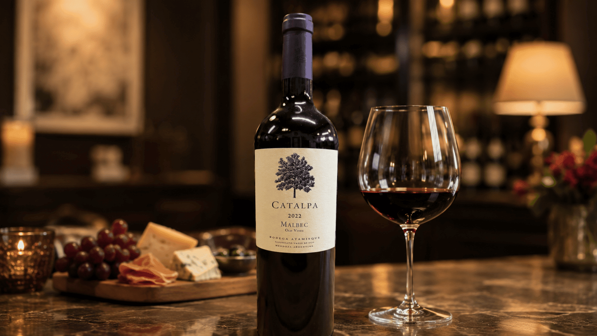 malbec wine bottle beside a red wine glass with grapes, cheese, and cured meat nearby