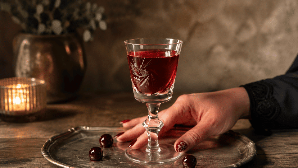Crystal glass of ruby Marsala wine on a silver tray with cherries and a hand nearby