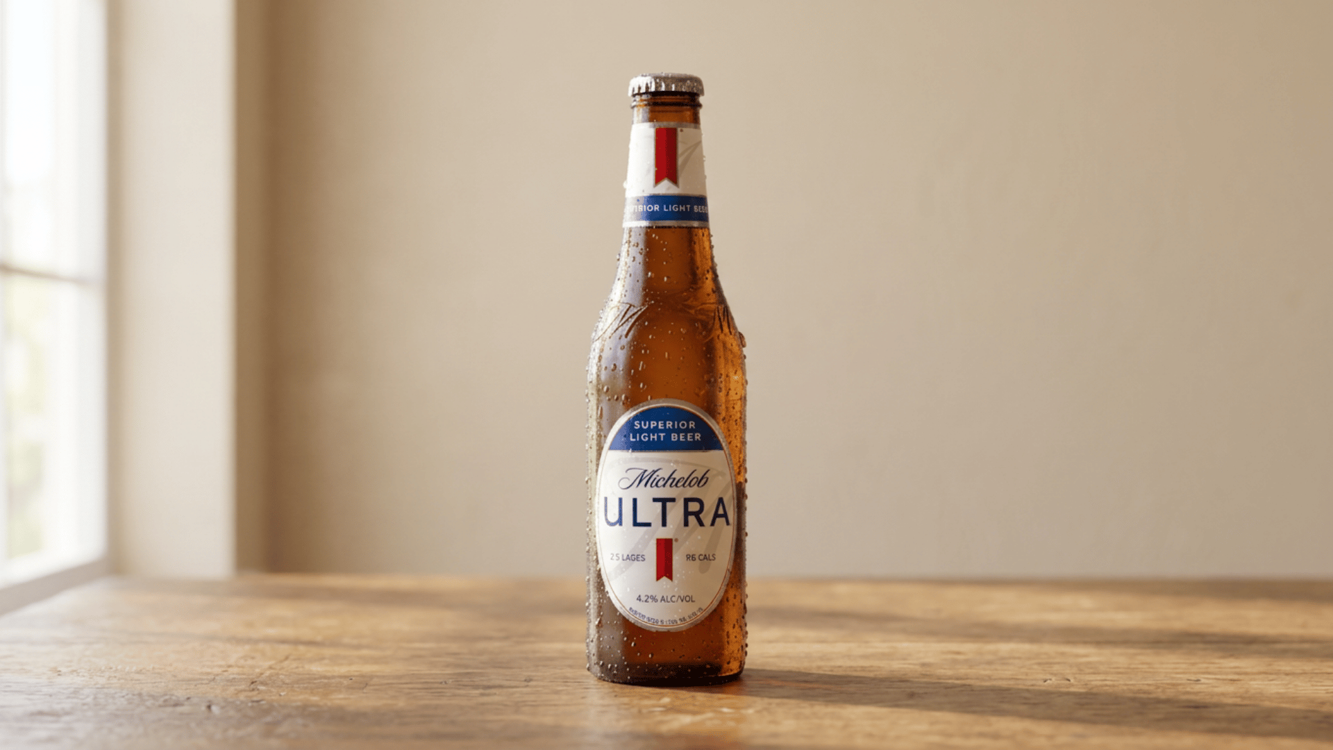 Michelob Ultra bottle with water droplets on wooden surface and soft light.