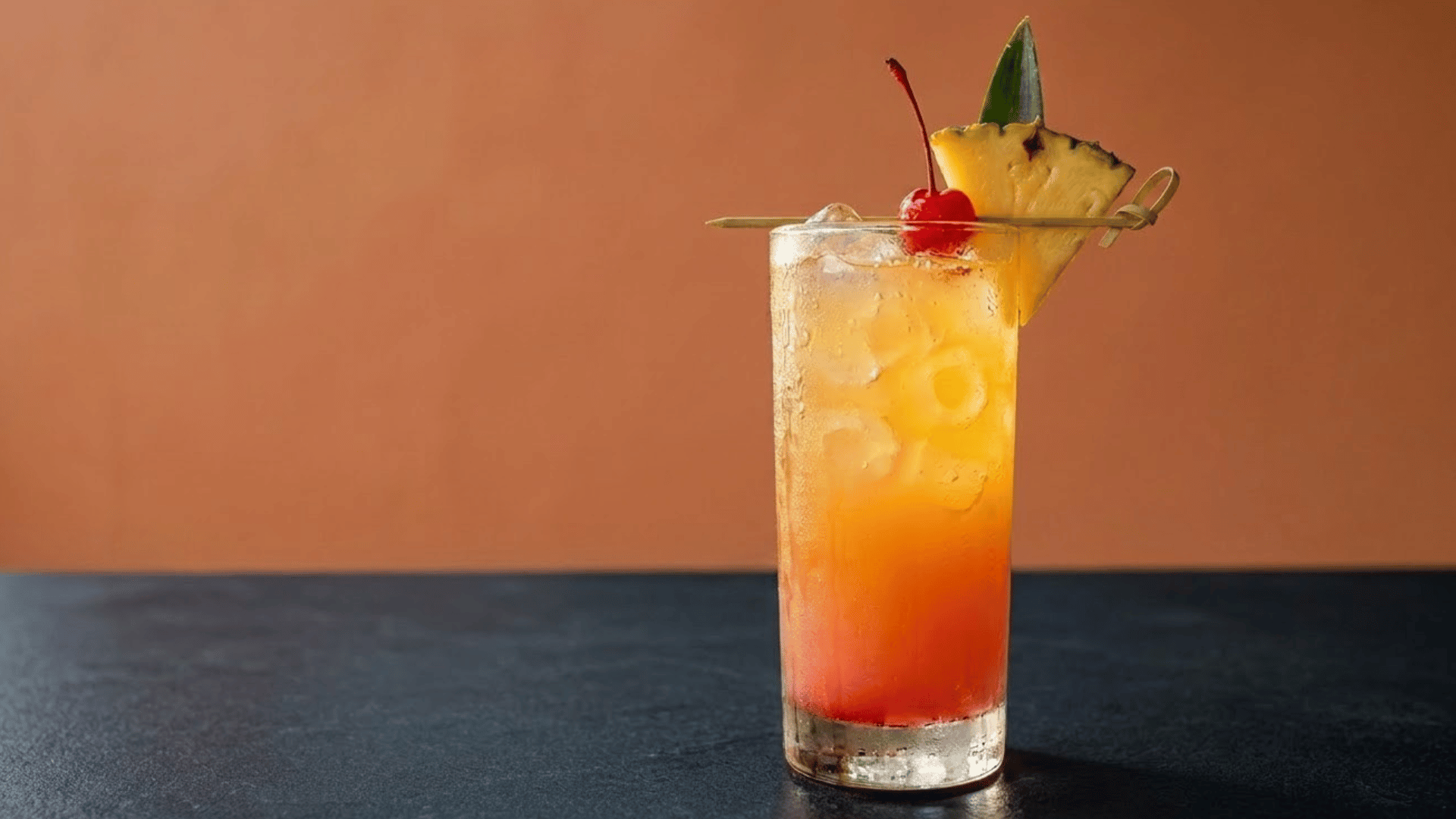 pineapple rum punch with ice, cherry, and pineapple garnish on a dark table