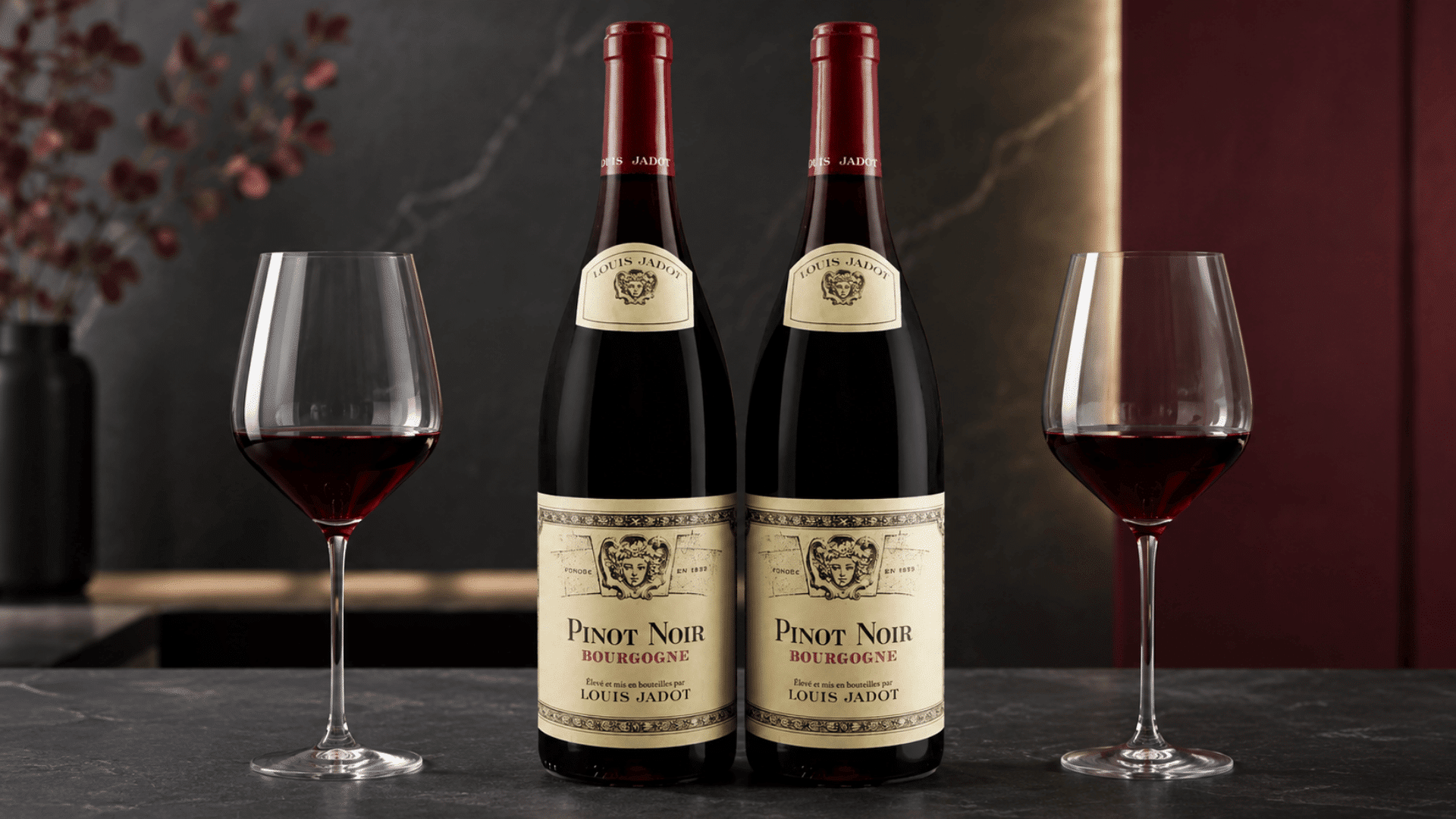 two pinot noir bottles placed between red wine glasses against a dark modern backdrop