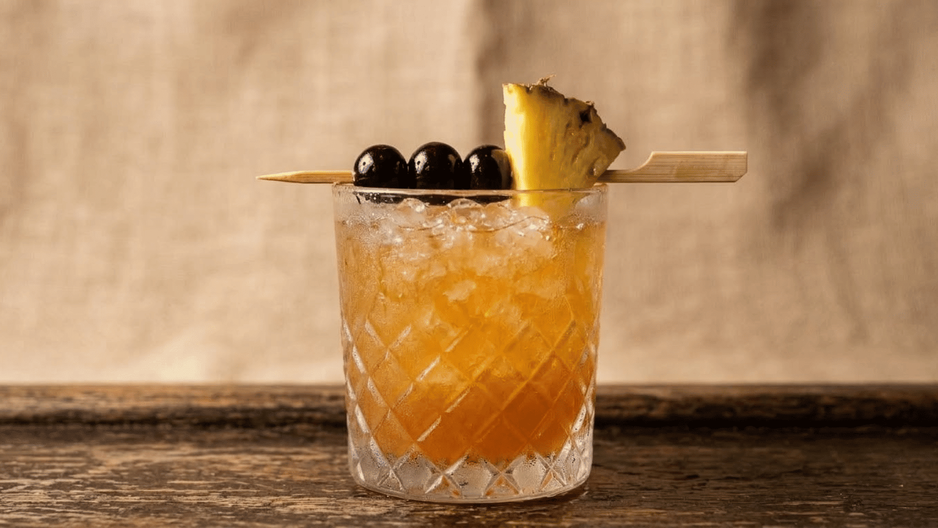 three dots and a dash cocktail garnished with a pineapple wedge and three cherries clustered together on one skewer